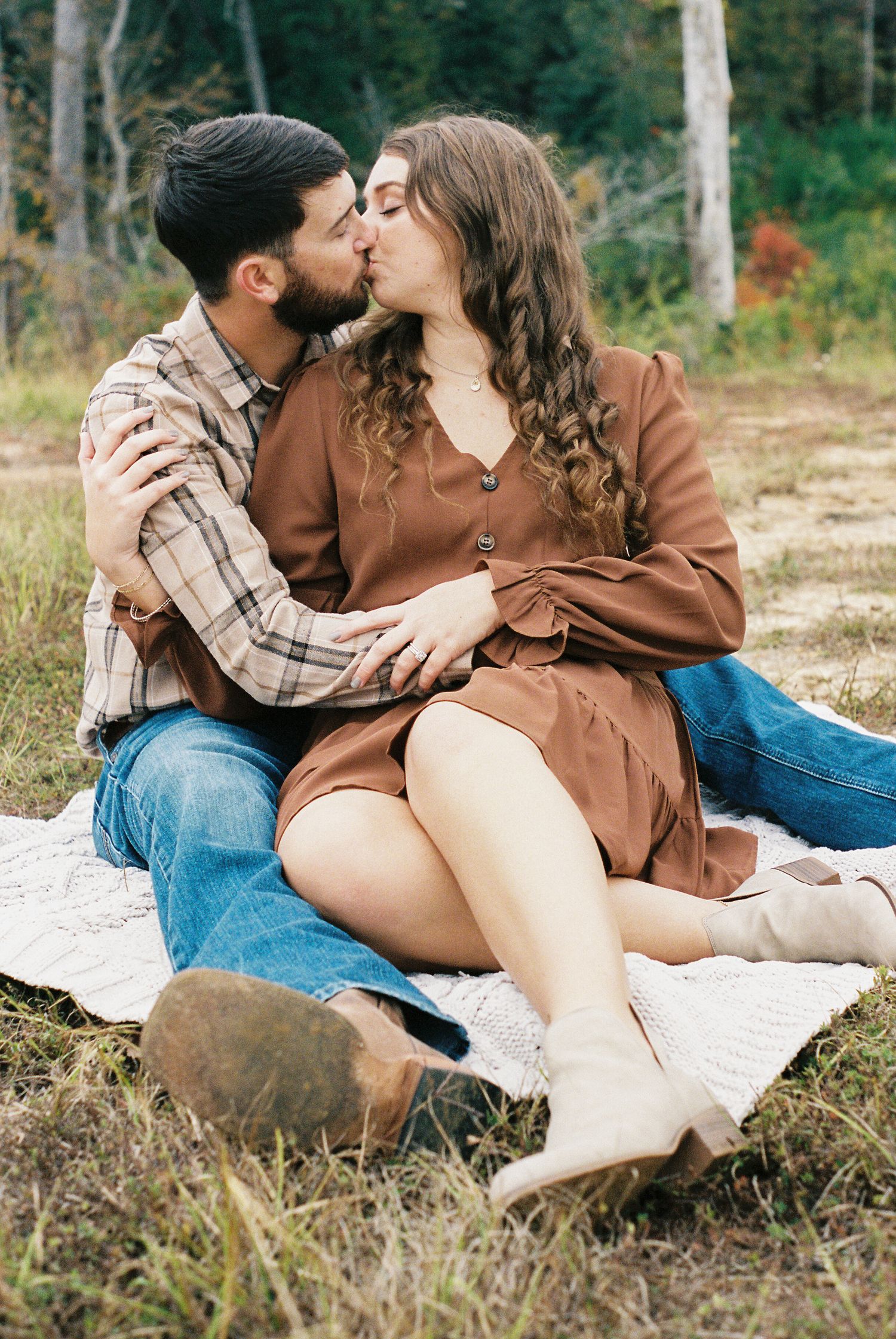 Couple sharing intimate moment on blanket in outdoor woodland setting.
