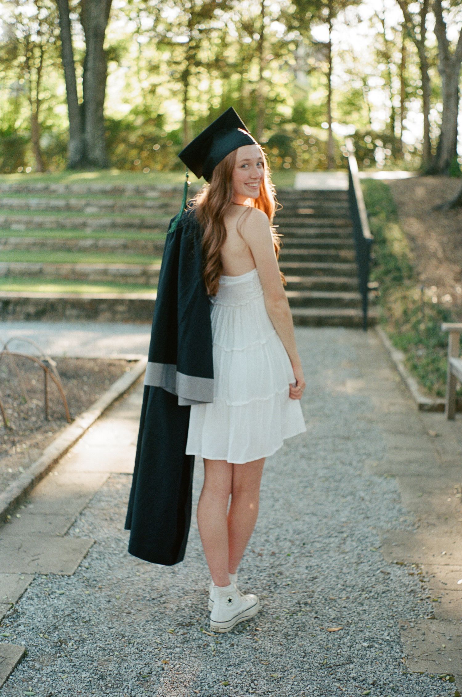 Graduation photos on a stone path showing someone in a white dress and black cap and gown.