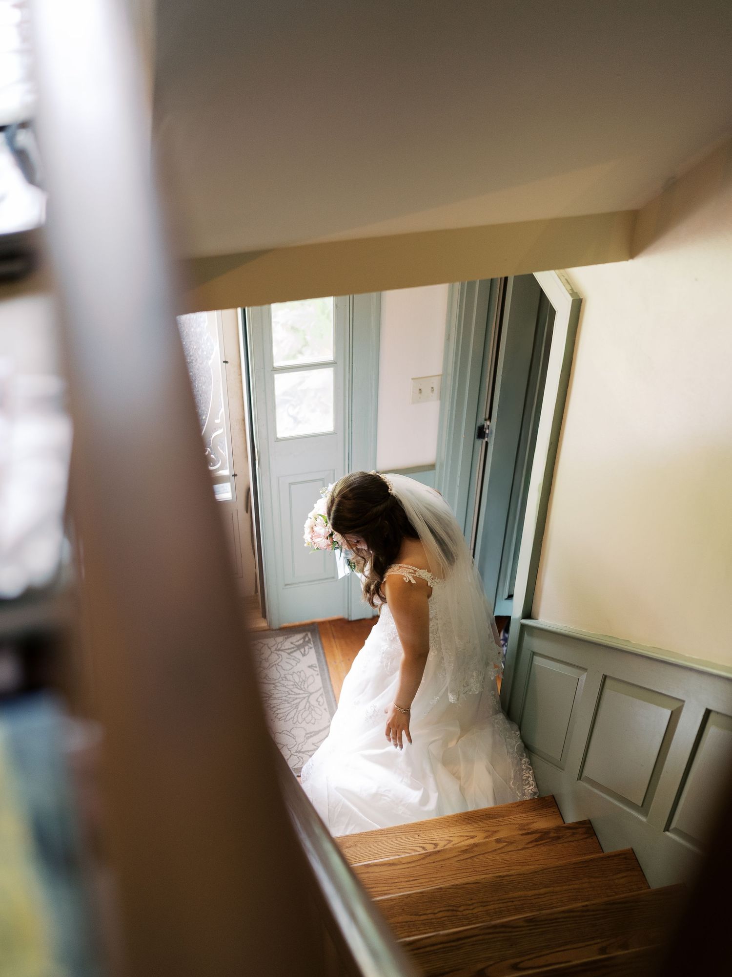 White wedding dress flowing down wooden stairs in soft natural light.