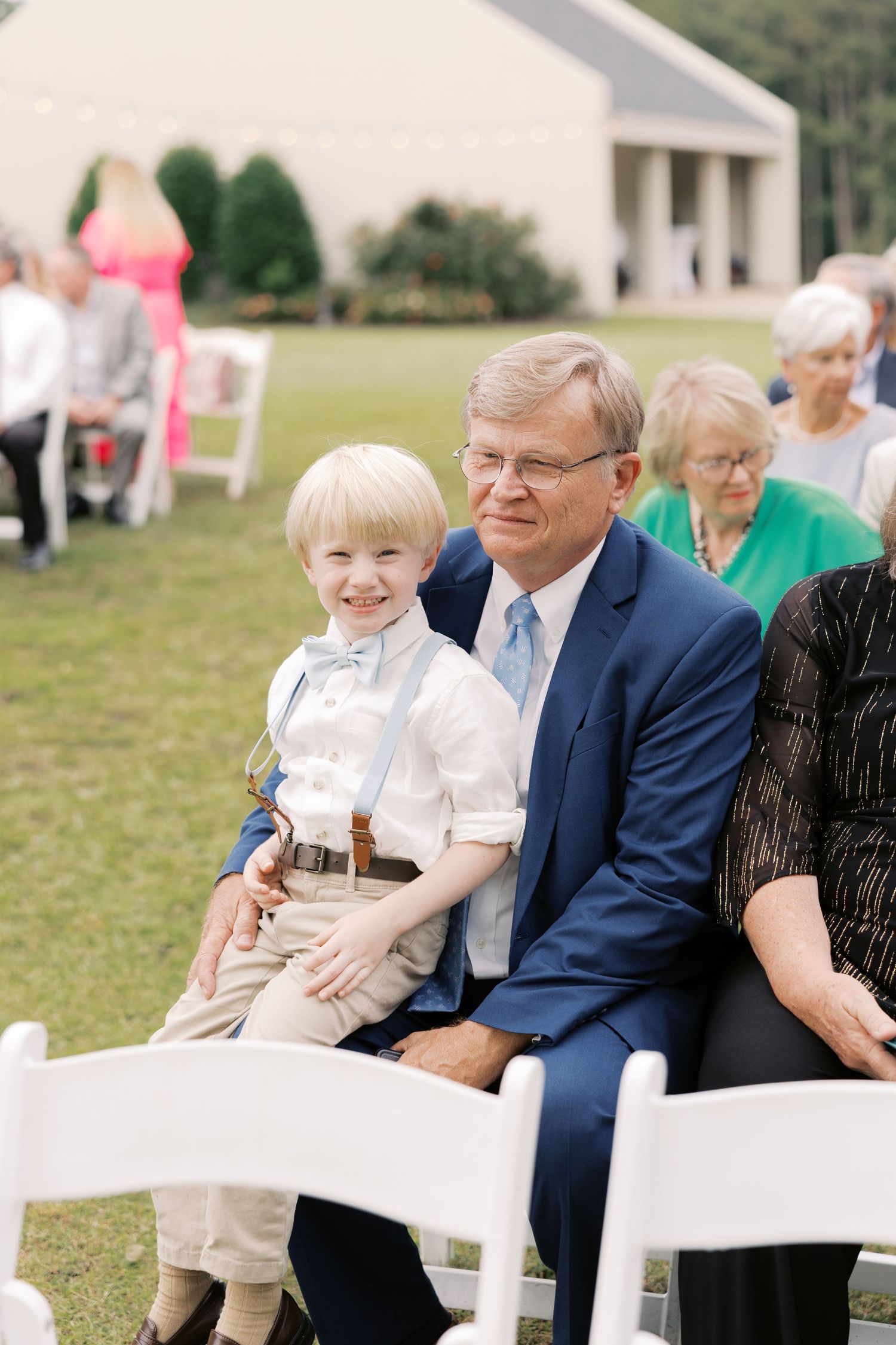 Wedding guests seated in white chairs at an outdoor ceremony.