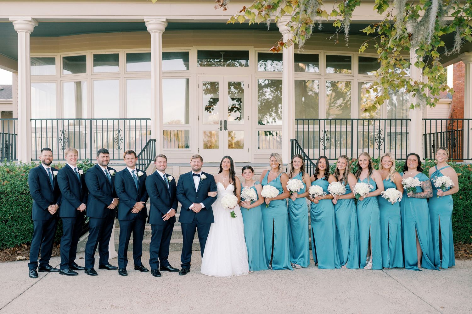 Wedding party in navy suits and turquoise dresses posed along a columned porch.