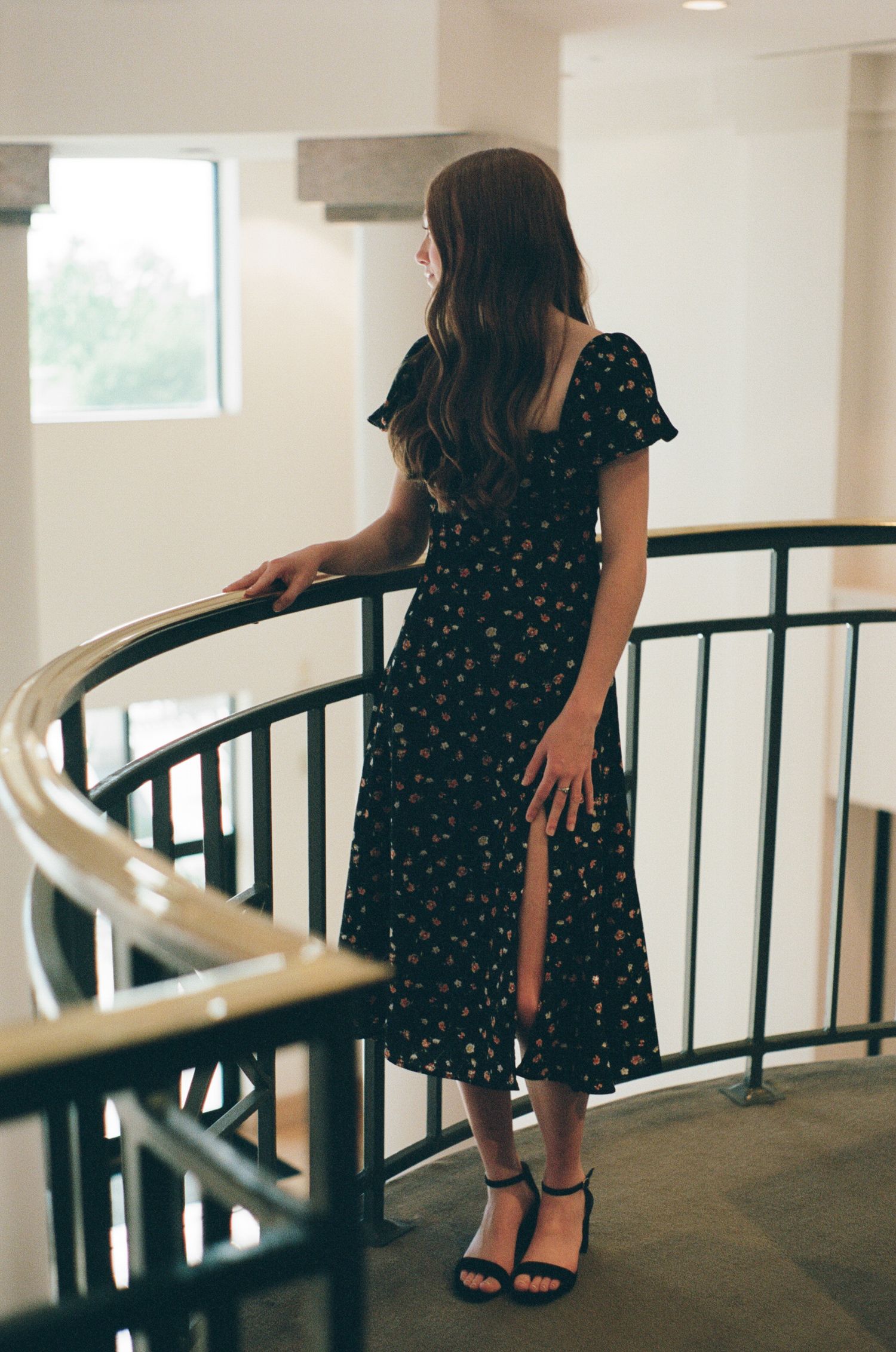 Person in polka dot dress walking along curved railing in bright interior space.