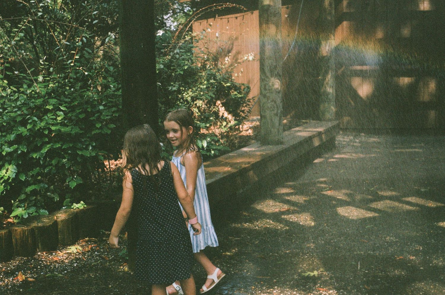 Children walking along a shaded pathway surrounded by trees and dappled sunlight.