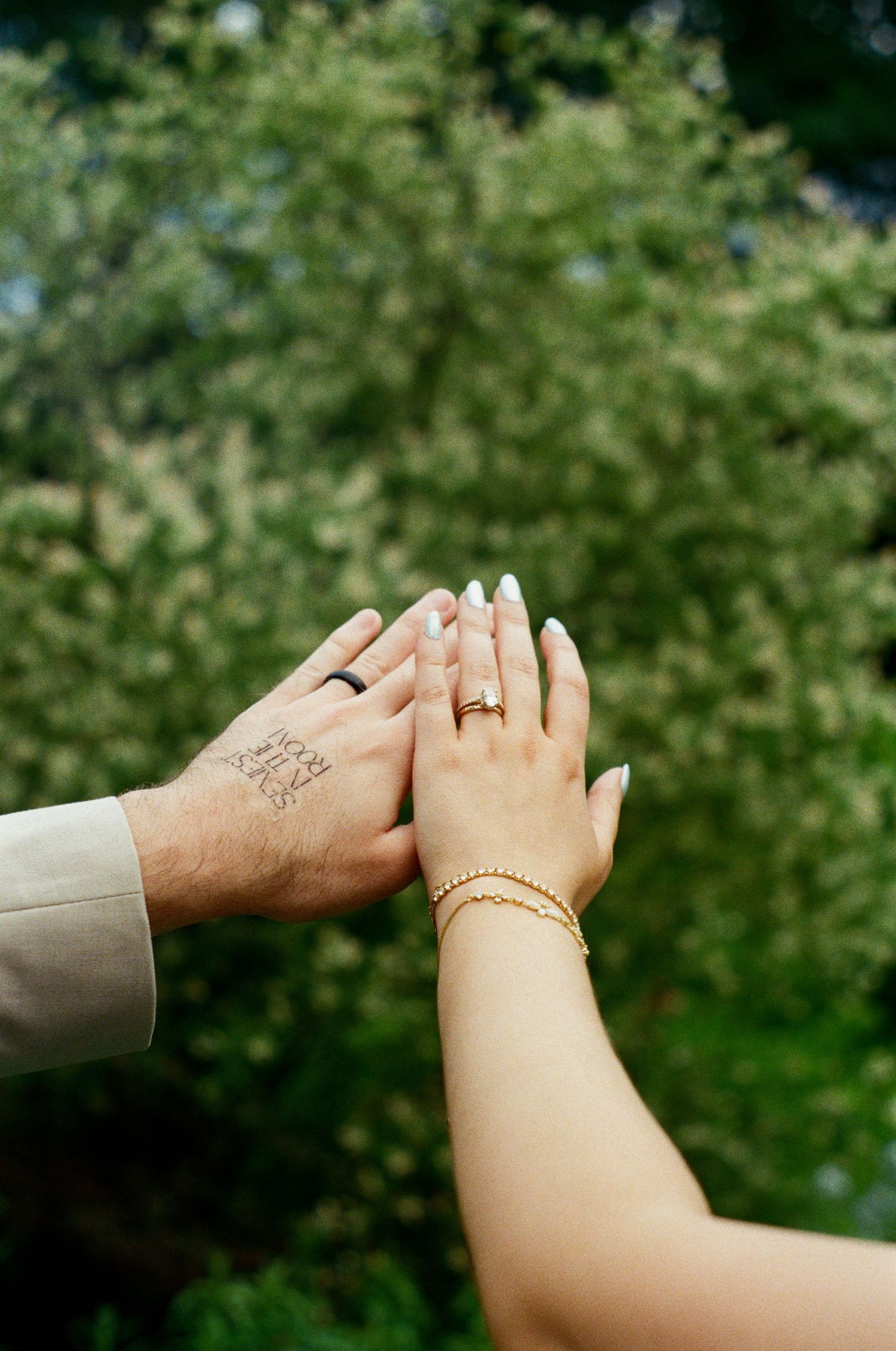 Close-up shots of hands holding each other showing rings and tattoos against a green outdoor background.