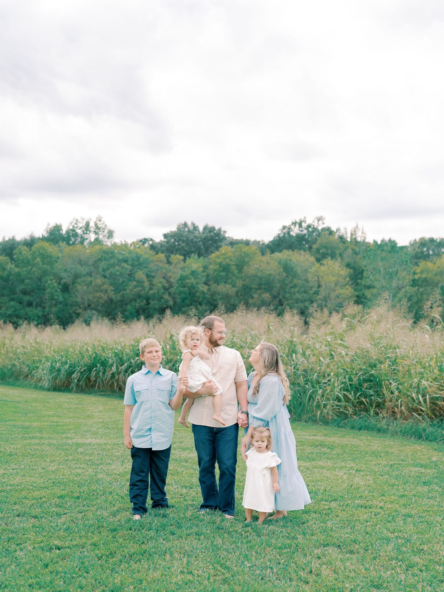 Family members walk together across a green field during a summer photo session.