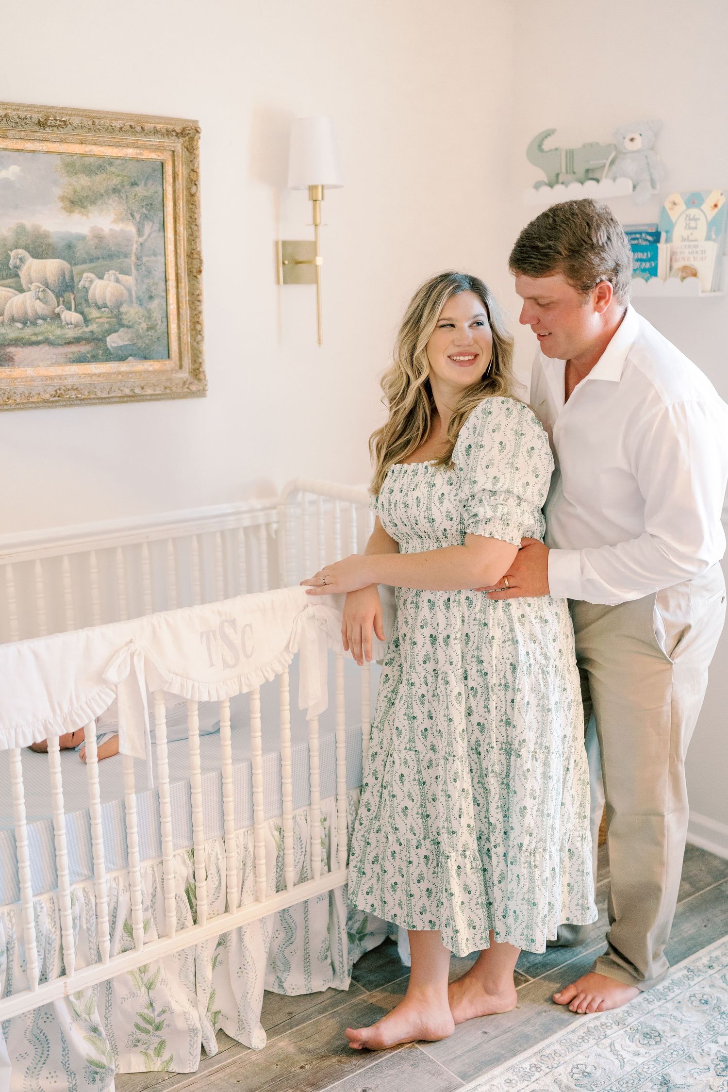 Couple shares joyful moments in nursery decorated with white furniture and framed artwork.