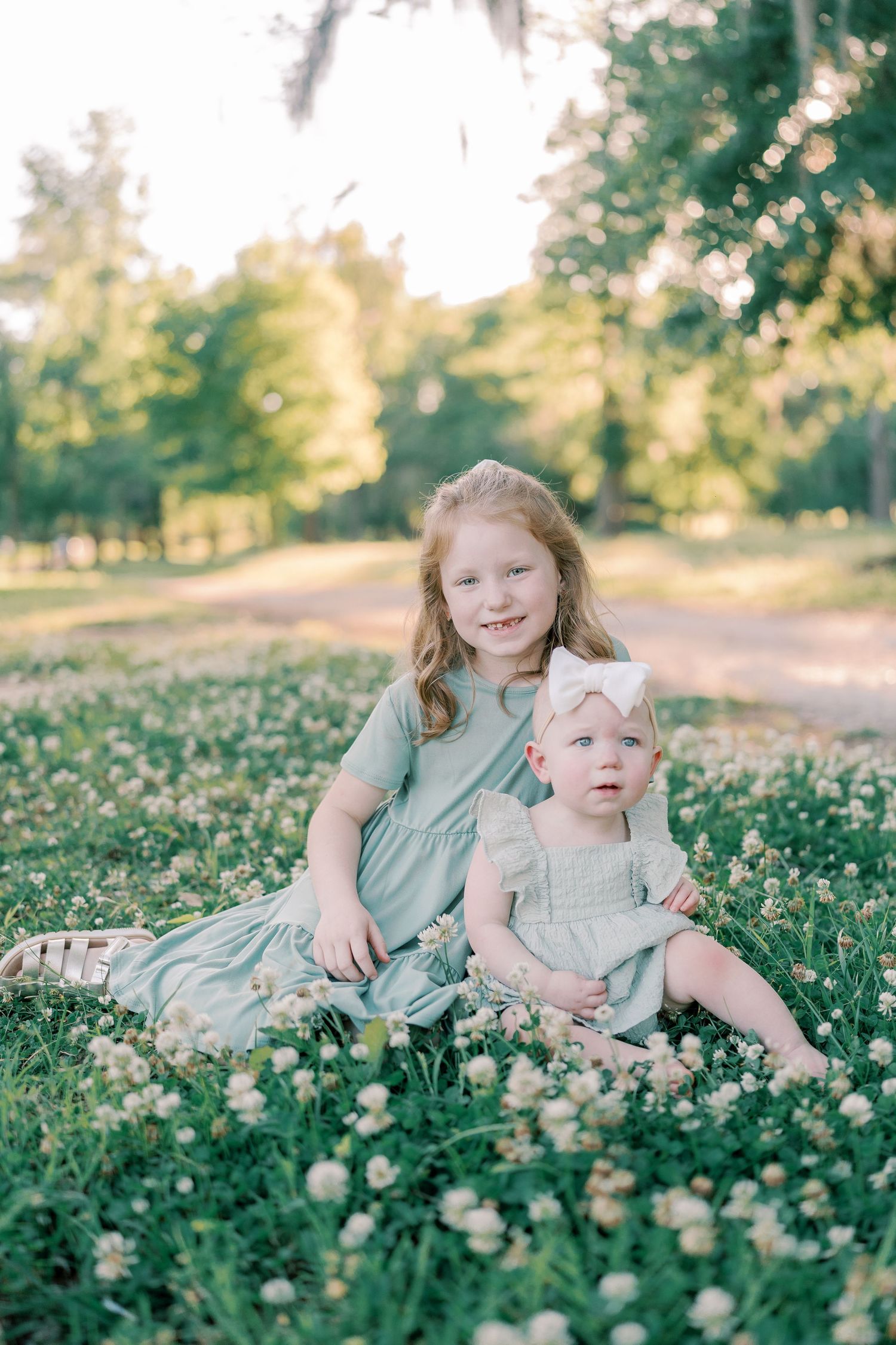 Two siblings pose together in a field of white wildflowers during a summer photo session.