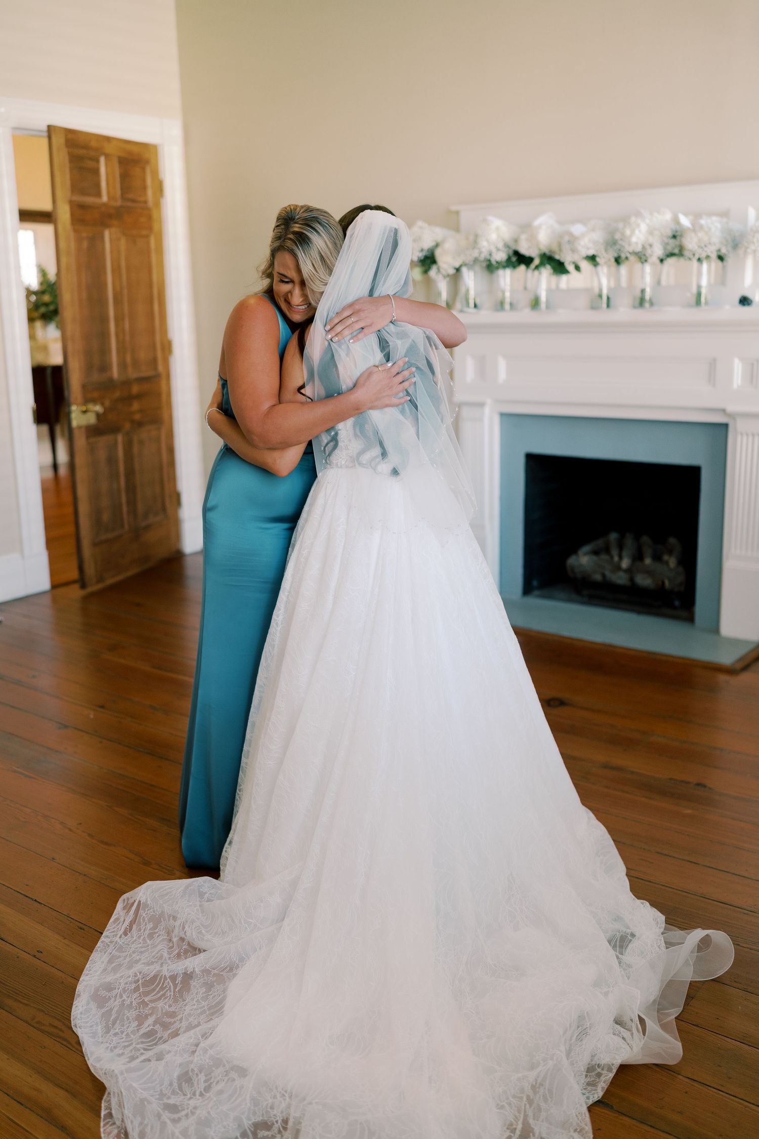 Candid wedding preparation moment captured in a room with white walls and wooden floors.