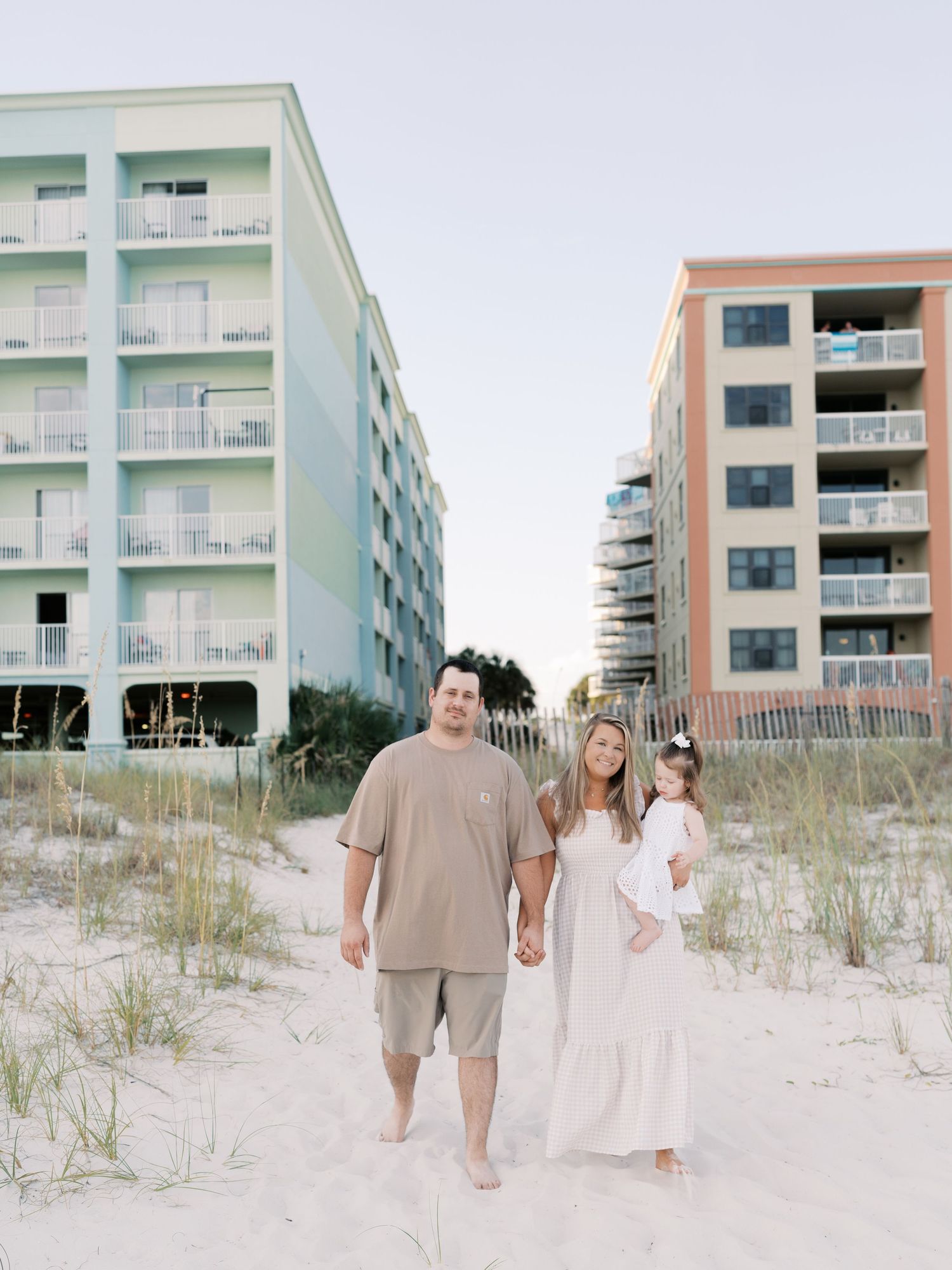 Beachgoers walking near pastel-colored beach condominiums with sea oats growing in sandy dunes.