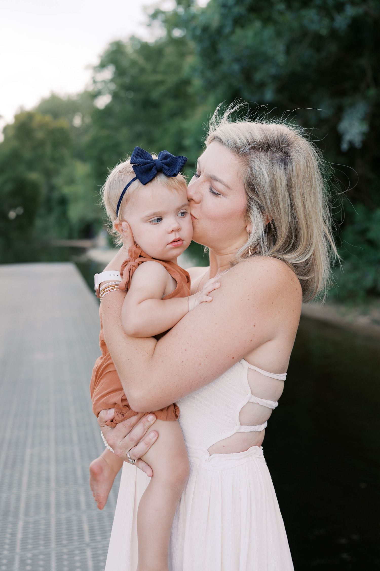 A tender moment between parent and baby in matching white outfits against a natural outdoor backdrop.