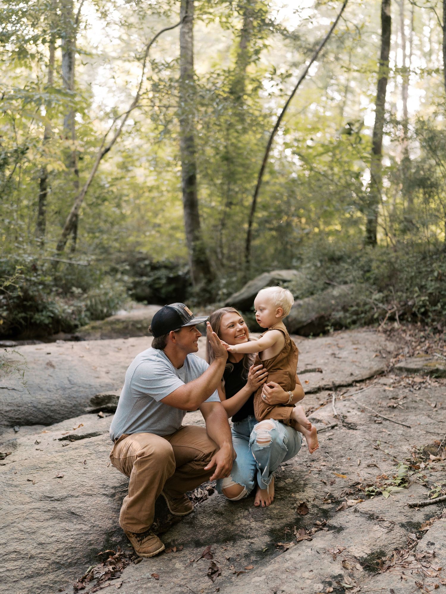 A family plays together on the ground in a peaceful forest setting.