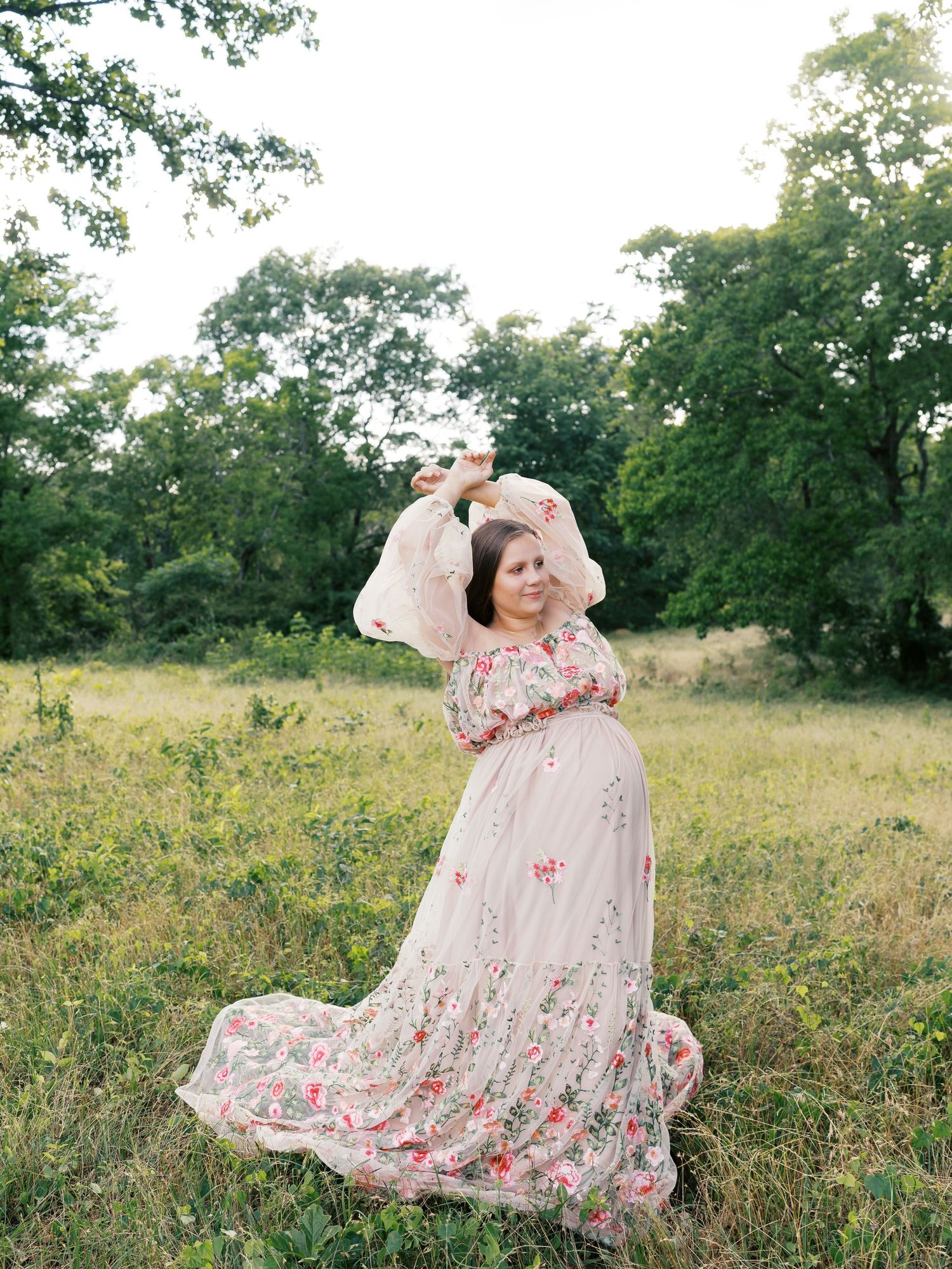 Woman in floral dress poses gracefully in a sunlit meadow during outdoor photo session.