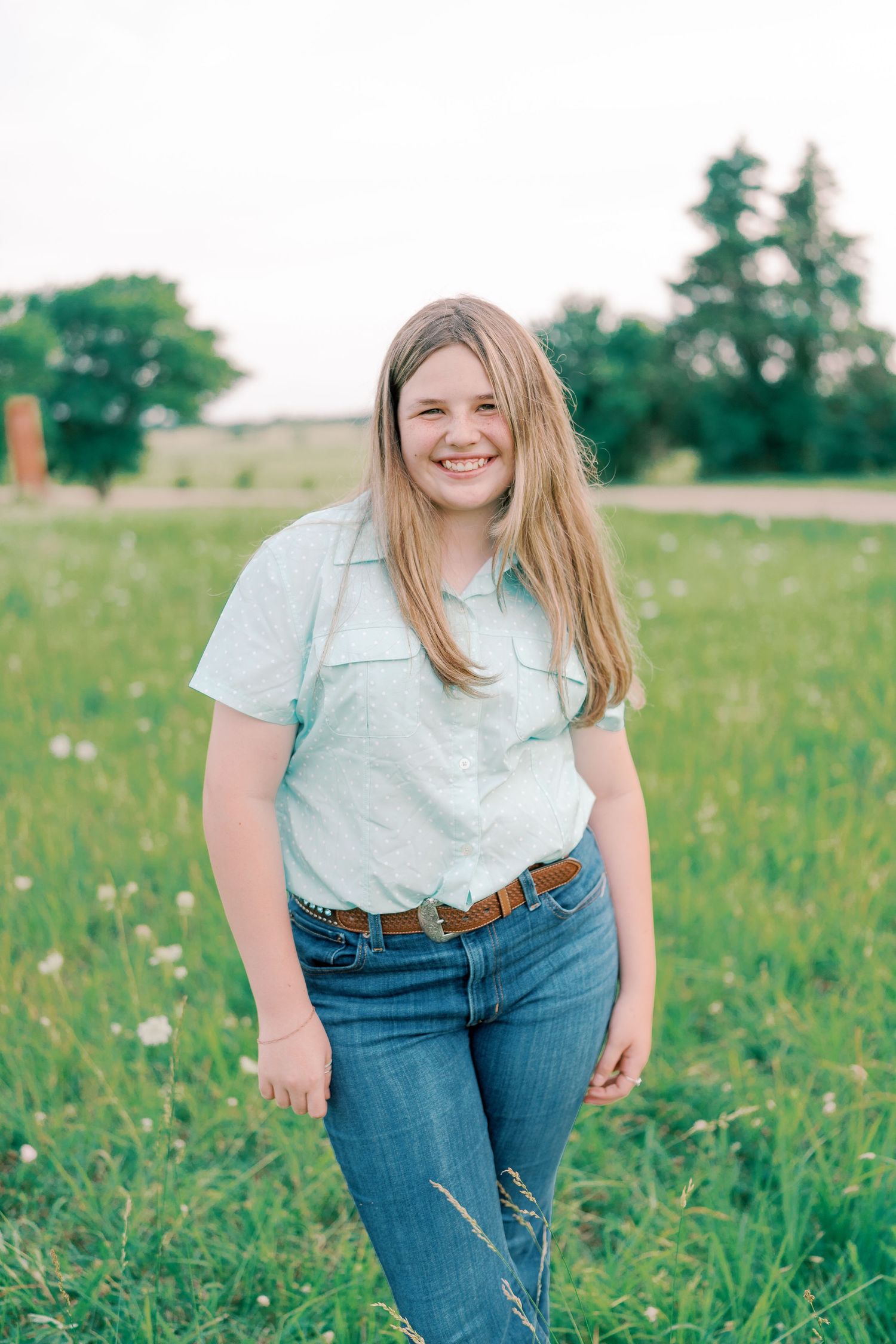 Person in light blue shirt and jeans poses in a sunny wildflower meadow.