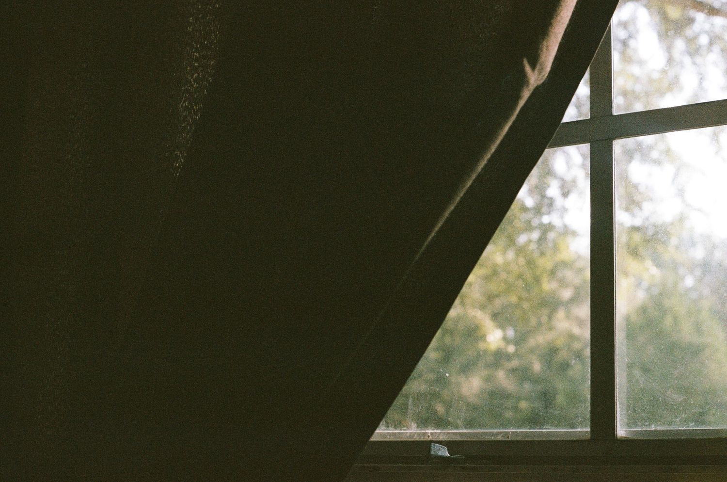 Sunlight streams through a dark curtained window creating dramatic shadows.