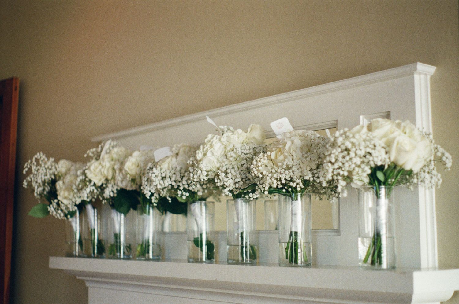 White floral arrangements line a decorative shelf at an elegant event.