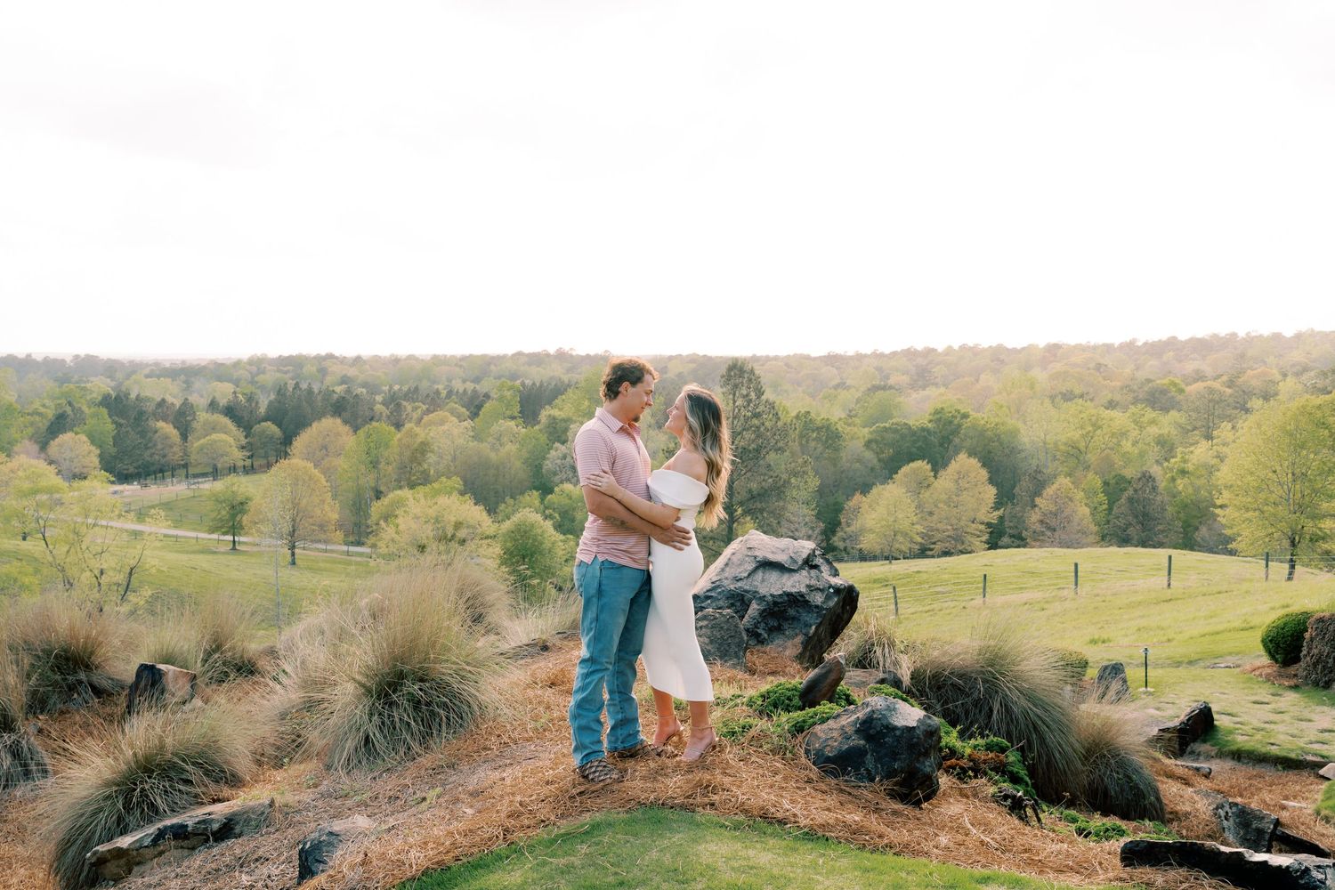 Romantic couple poses on hilltop with scenic countryside views in background.