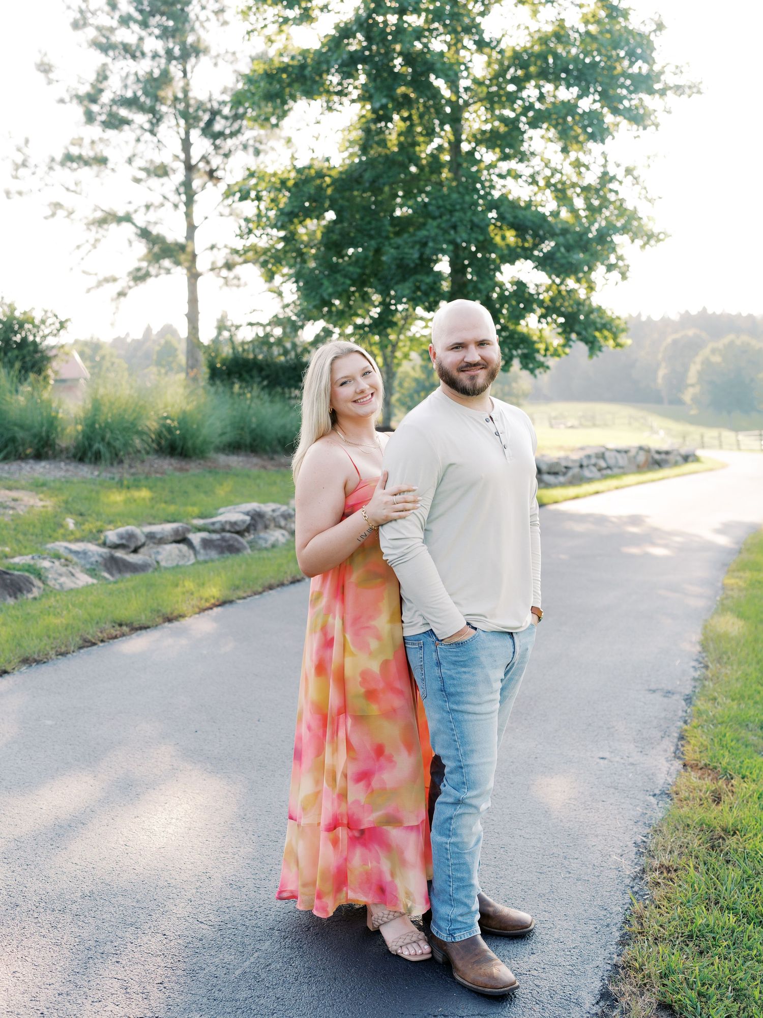 Couple in summer outfits walking along scenic path with stone wall and trees.