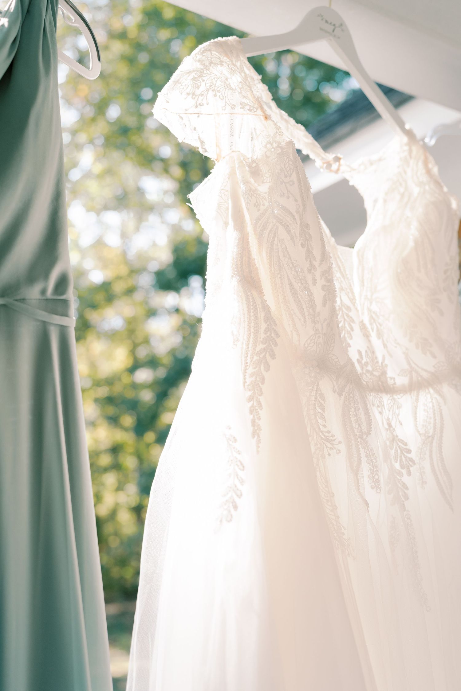 Close-up of lace white wedding gown and sage green bridesmaid dress detail.