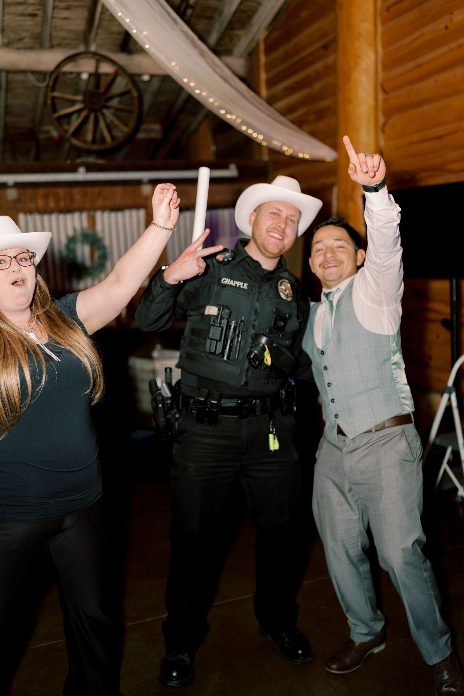 Law enforcement officers and guests dancing energetically at a celebration in a rustic wooden venue.