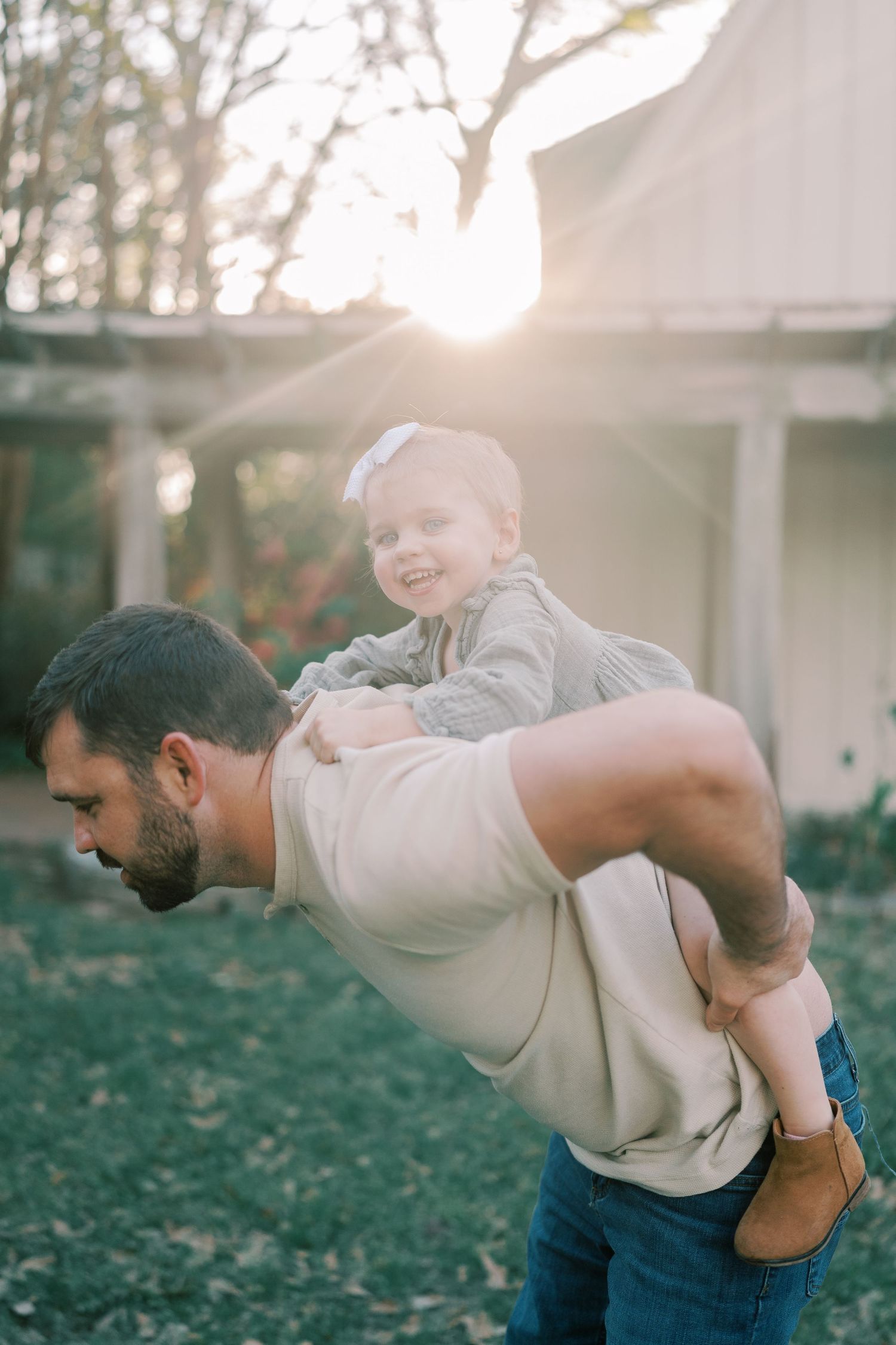 Playful family moment captured against a white building in golden evening light.