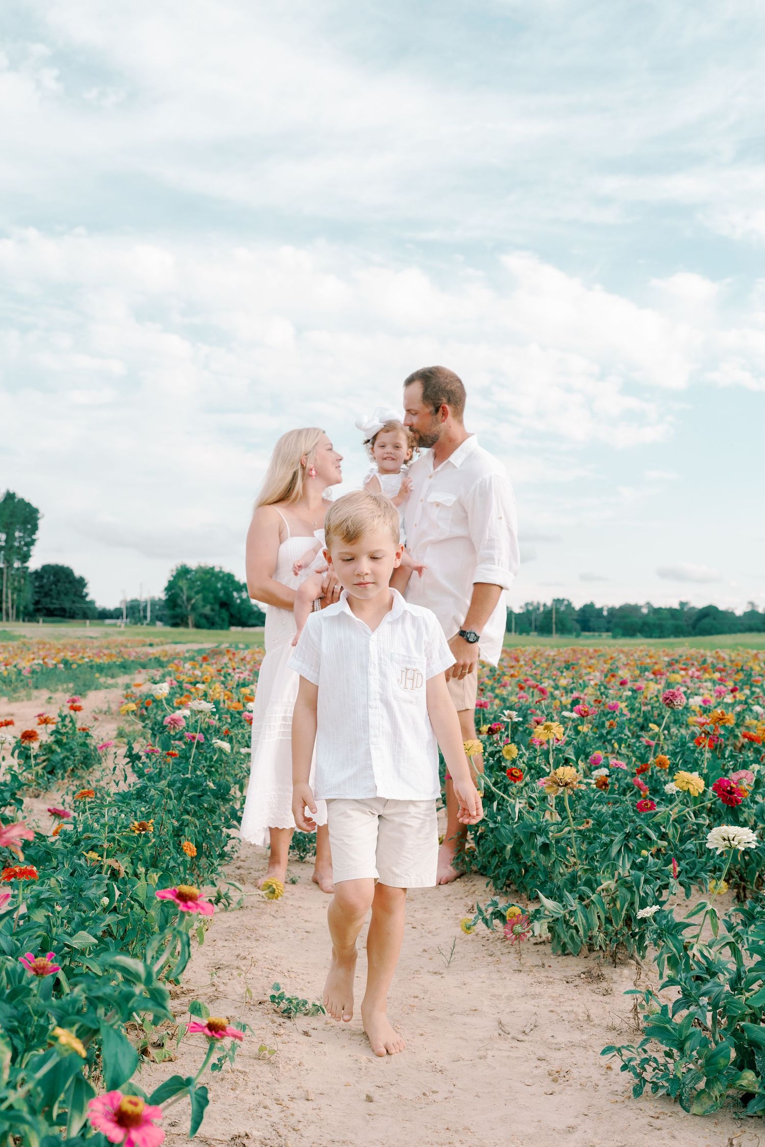 A group poses together on a dirt path through a colorful flower field under blue skies.