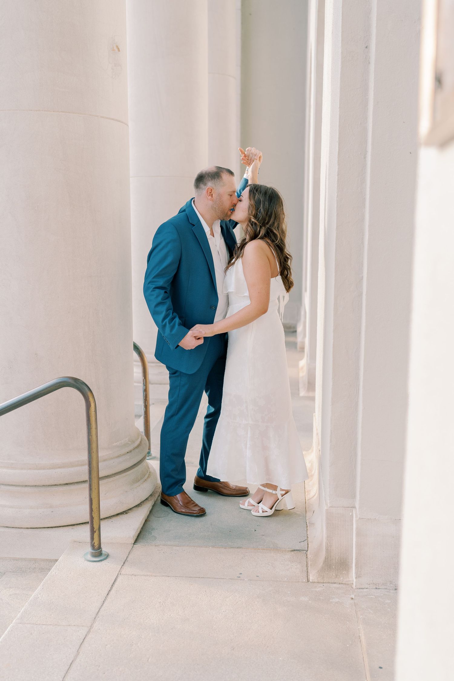 Romantic couple shares intimate moment between white columns of classic building.