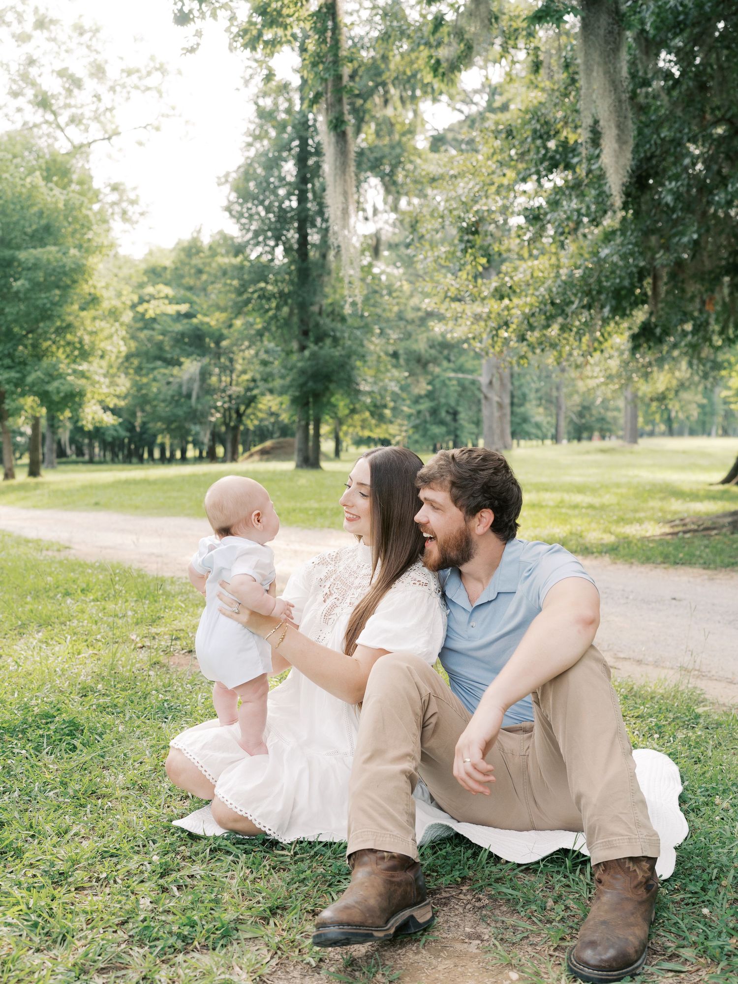 A family sits together on a grassy path in a sunlit park.