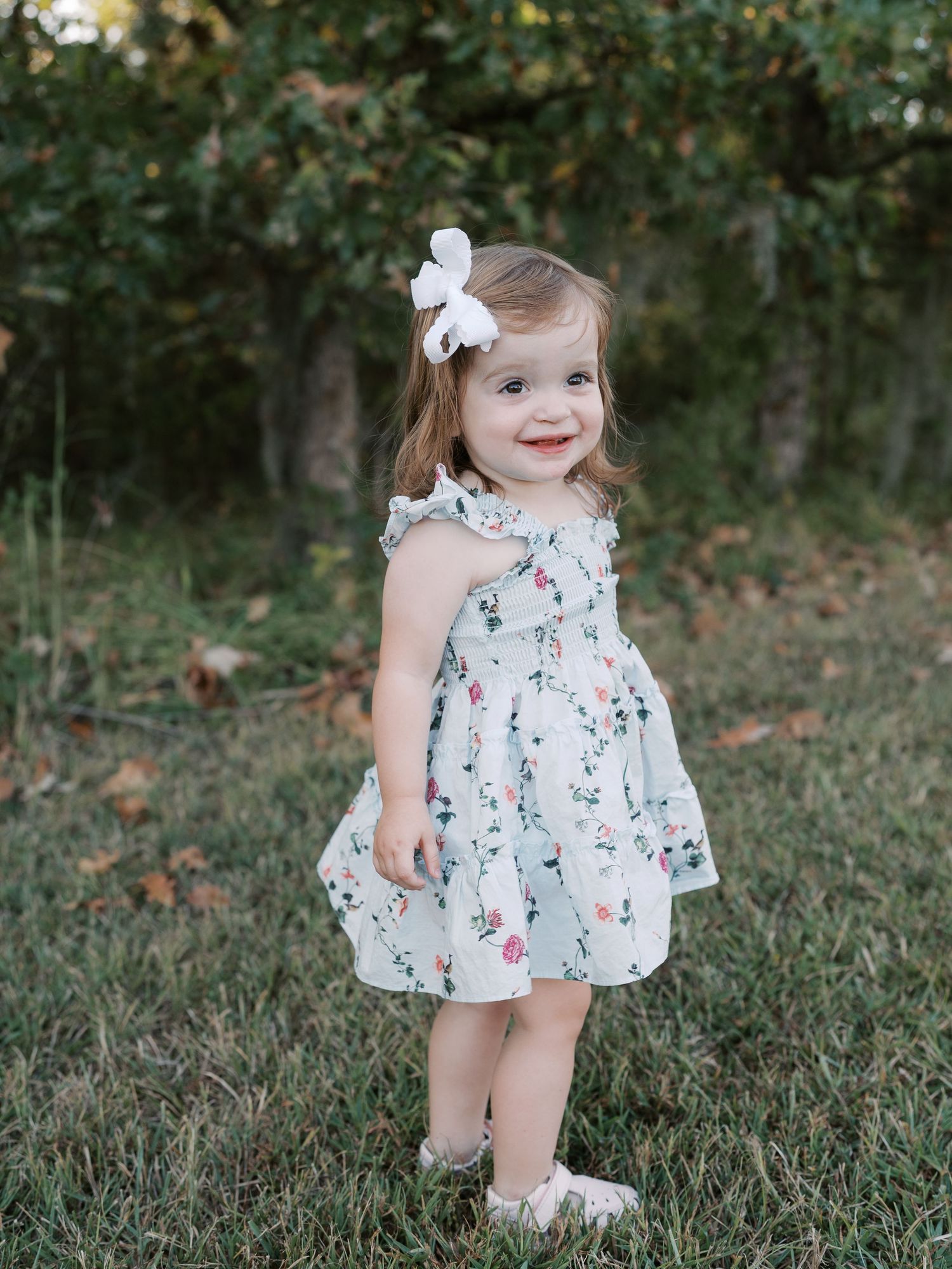 Young child in floral dress playing on grass during golden hour.