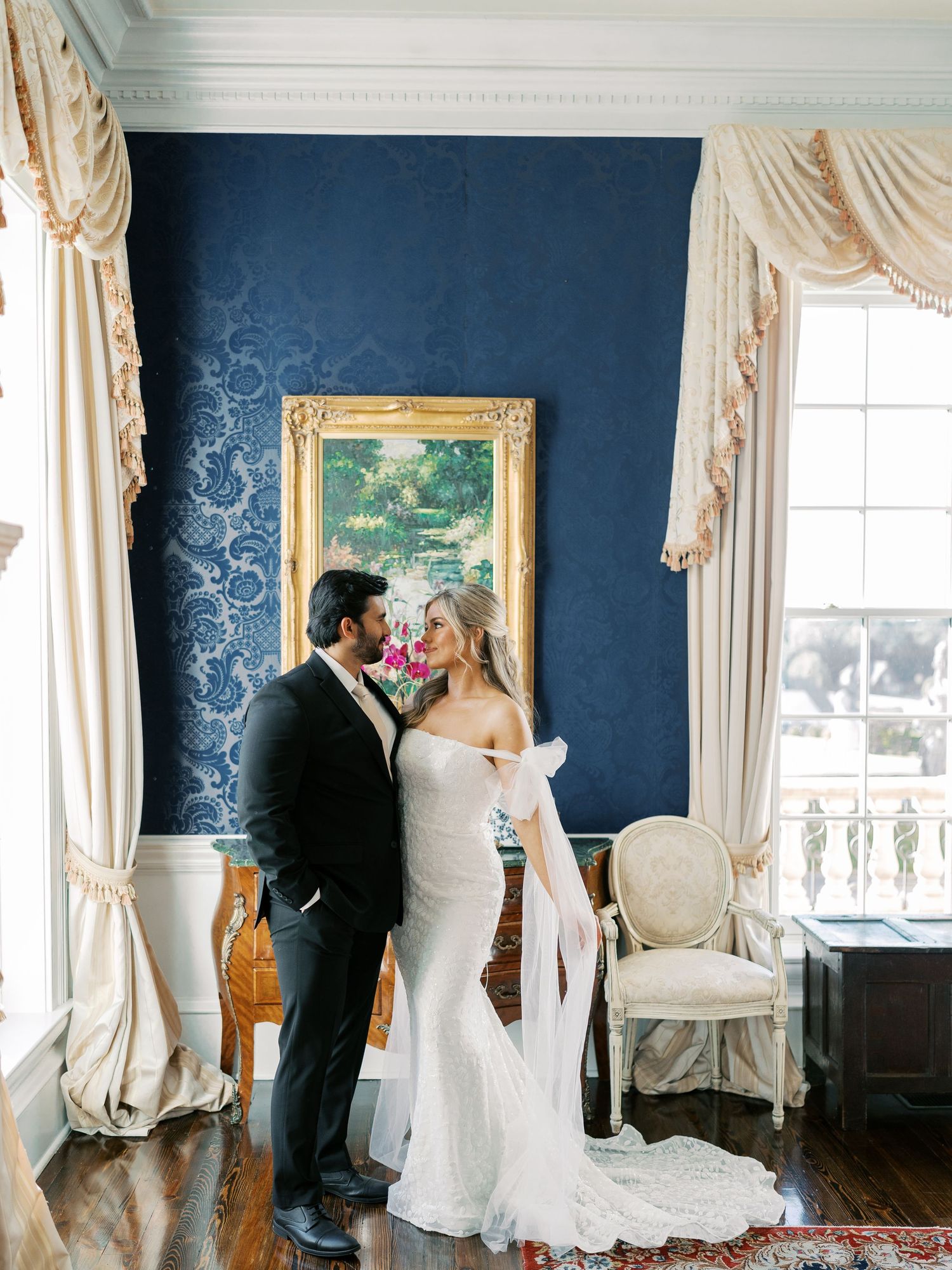 Wedding couple shares intimate moment in elegant room with navy walls and classic decor.
