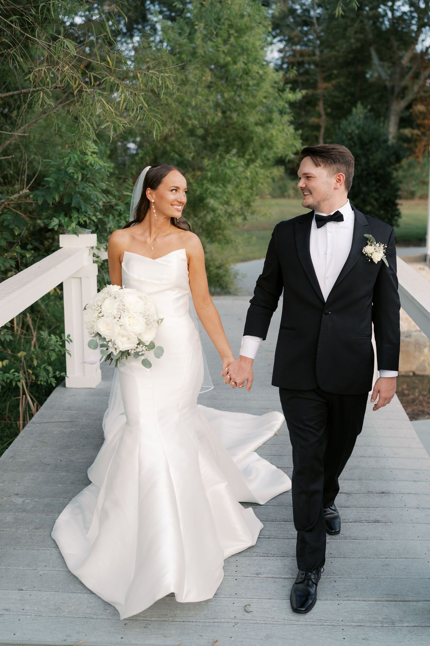 Newlyweds walking hand in hand on wooden boardwalk.
