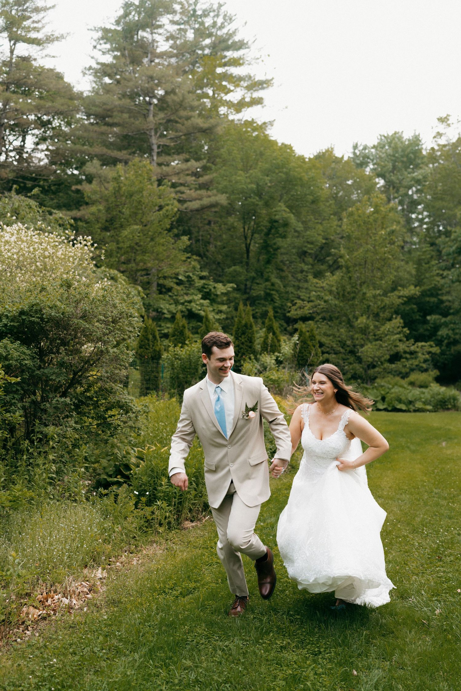 Playful newlyweds running through a lush green field during their wedding photoshoot.