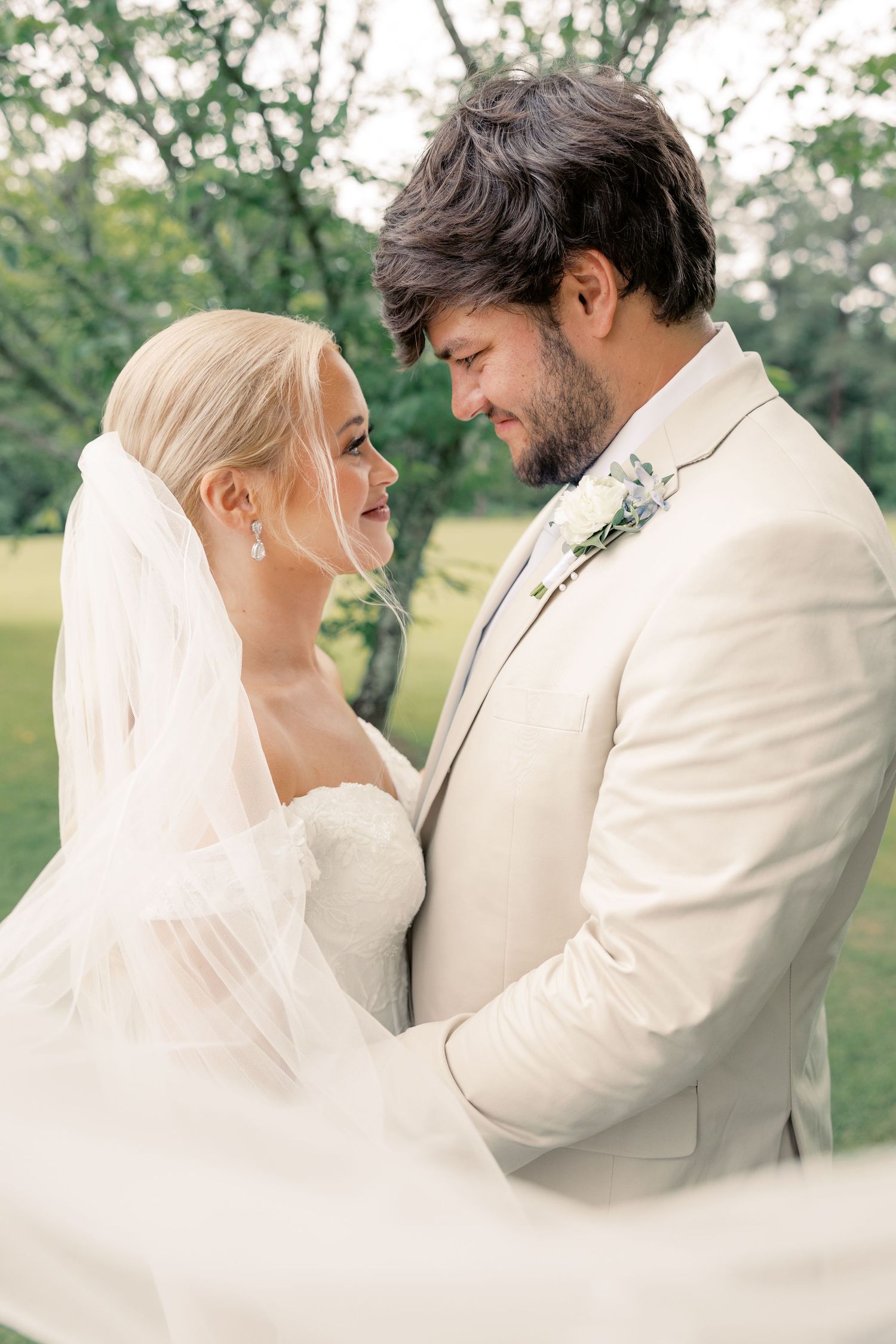 Romantic wedding couple embracing outdoors with flowing veil and cream suit.