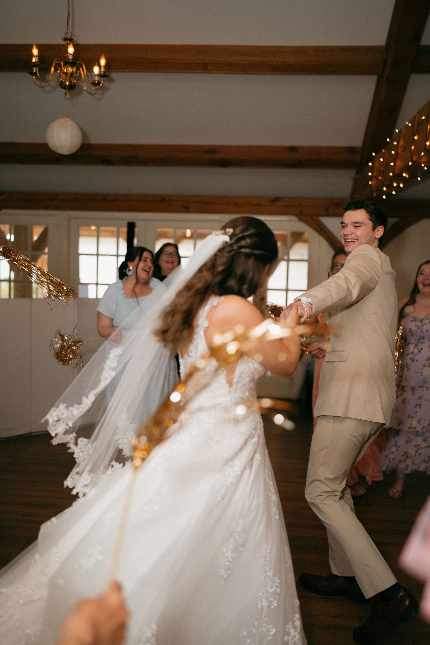 Wedding reception dance party with guests celebrating under string lights and chandeliers.