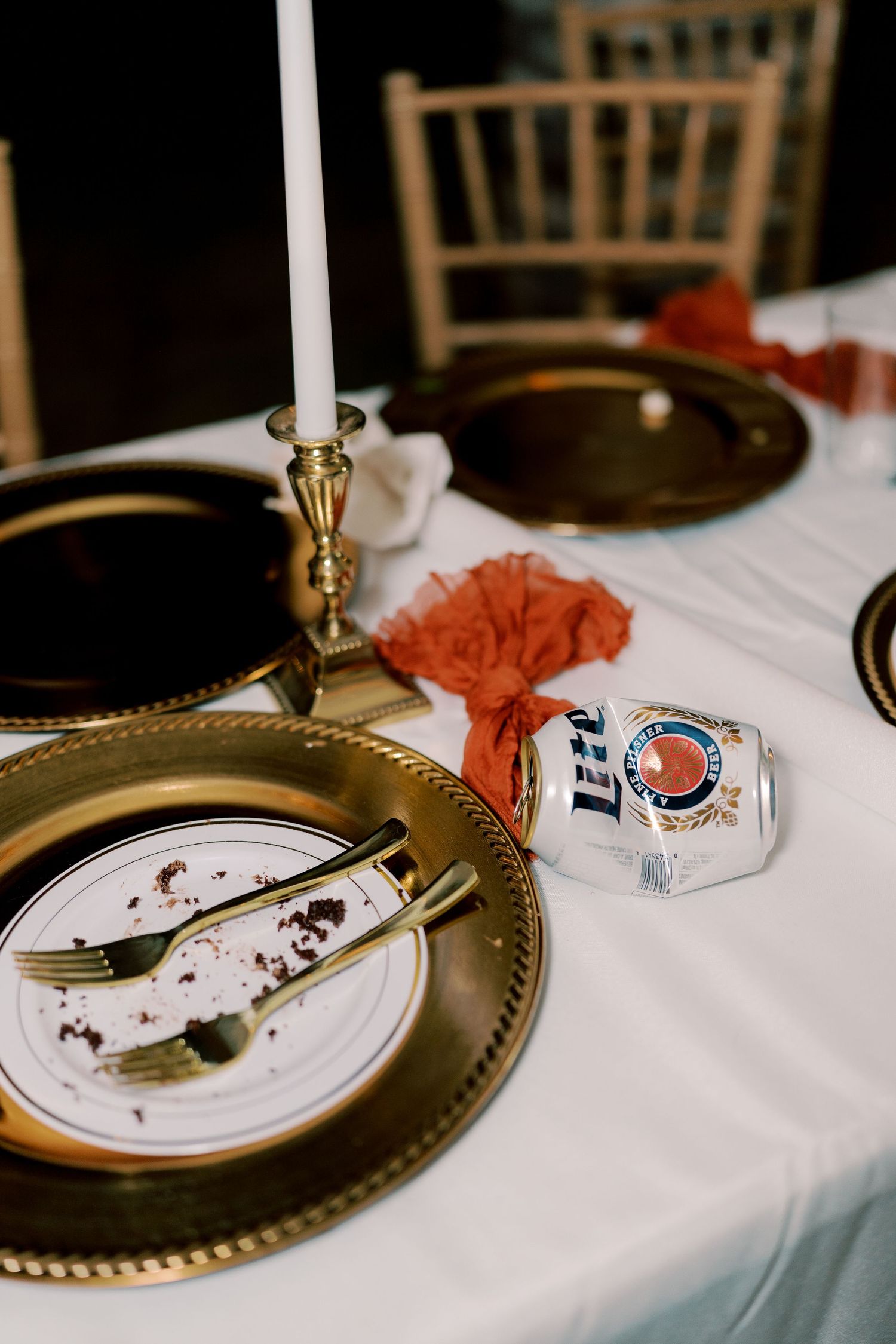Table setting with gold charger plates, candle holder and Miller Lite beer can at wedding reception.
