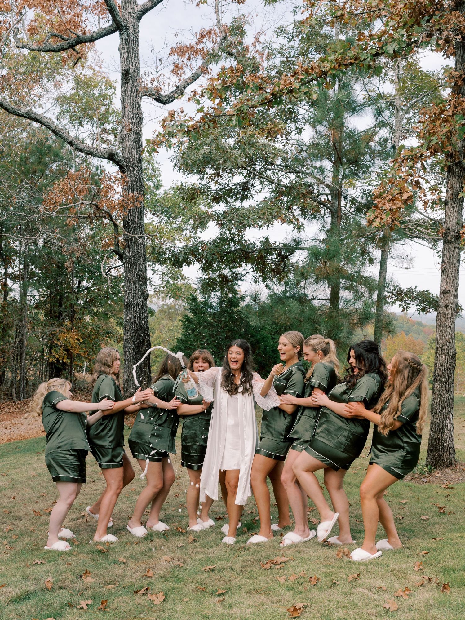Bridesmaids in olive green attire create fun domino effect pose on hillside.