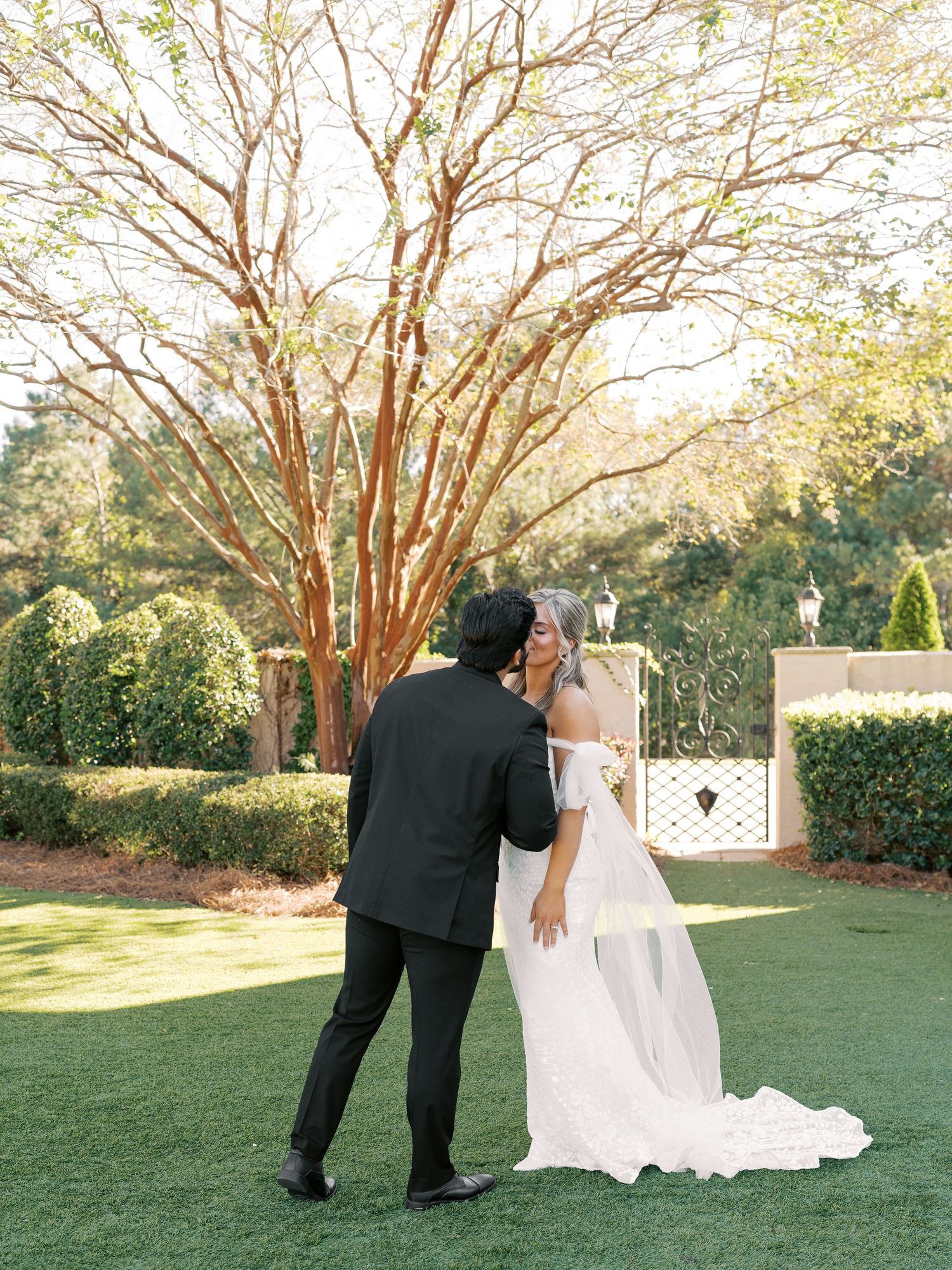 Couple embraces during outdoor wedding ceremony with beautiful garden backdrop.