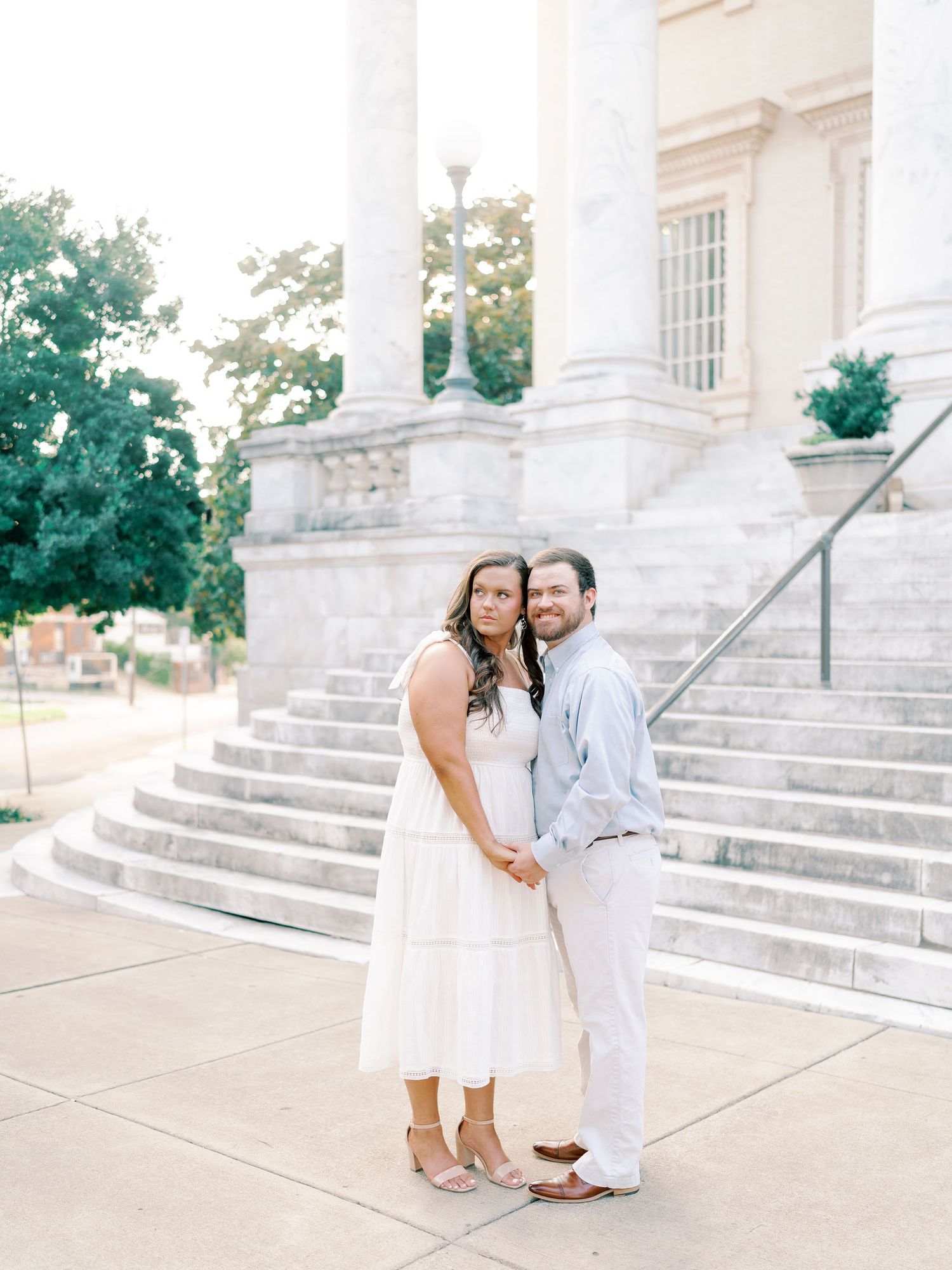 A couple shares intimate moments on grand white steps of a classical building.