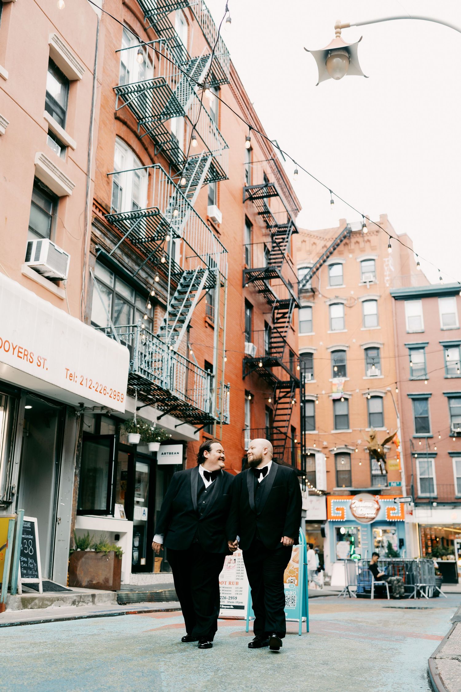 People walking along brick buildings with fire escapes in an urban neighborhood.