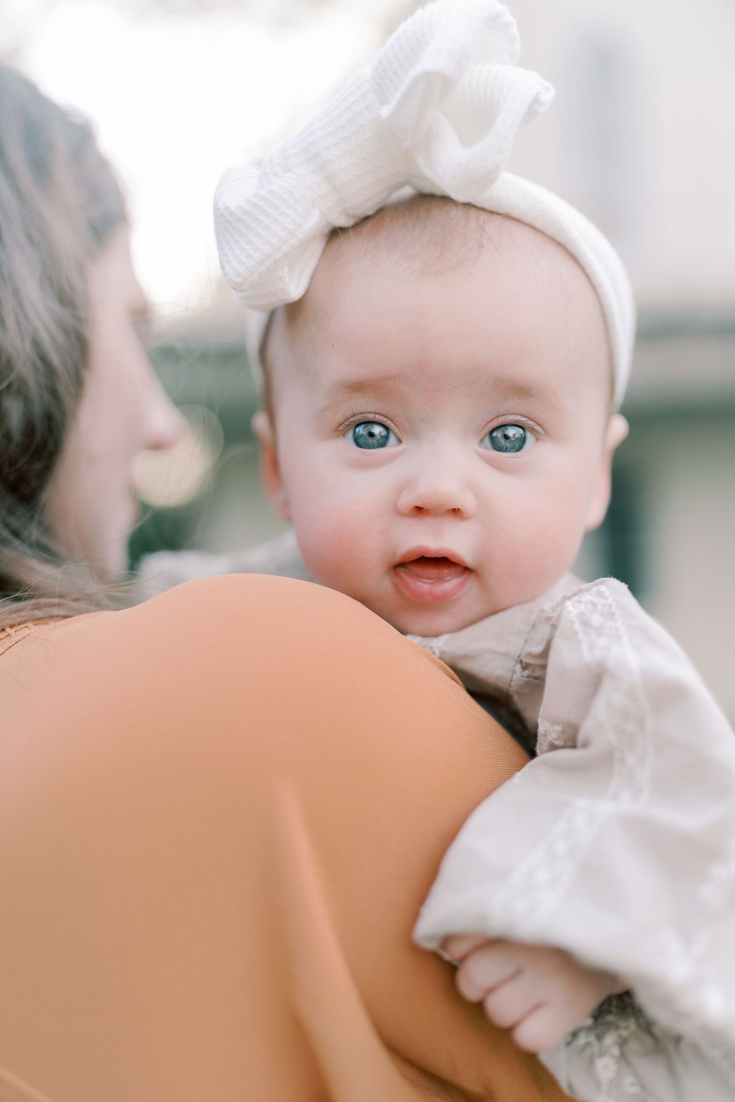 Close-up of bright blue eyes and white bow against a soft peach-colored background.