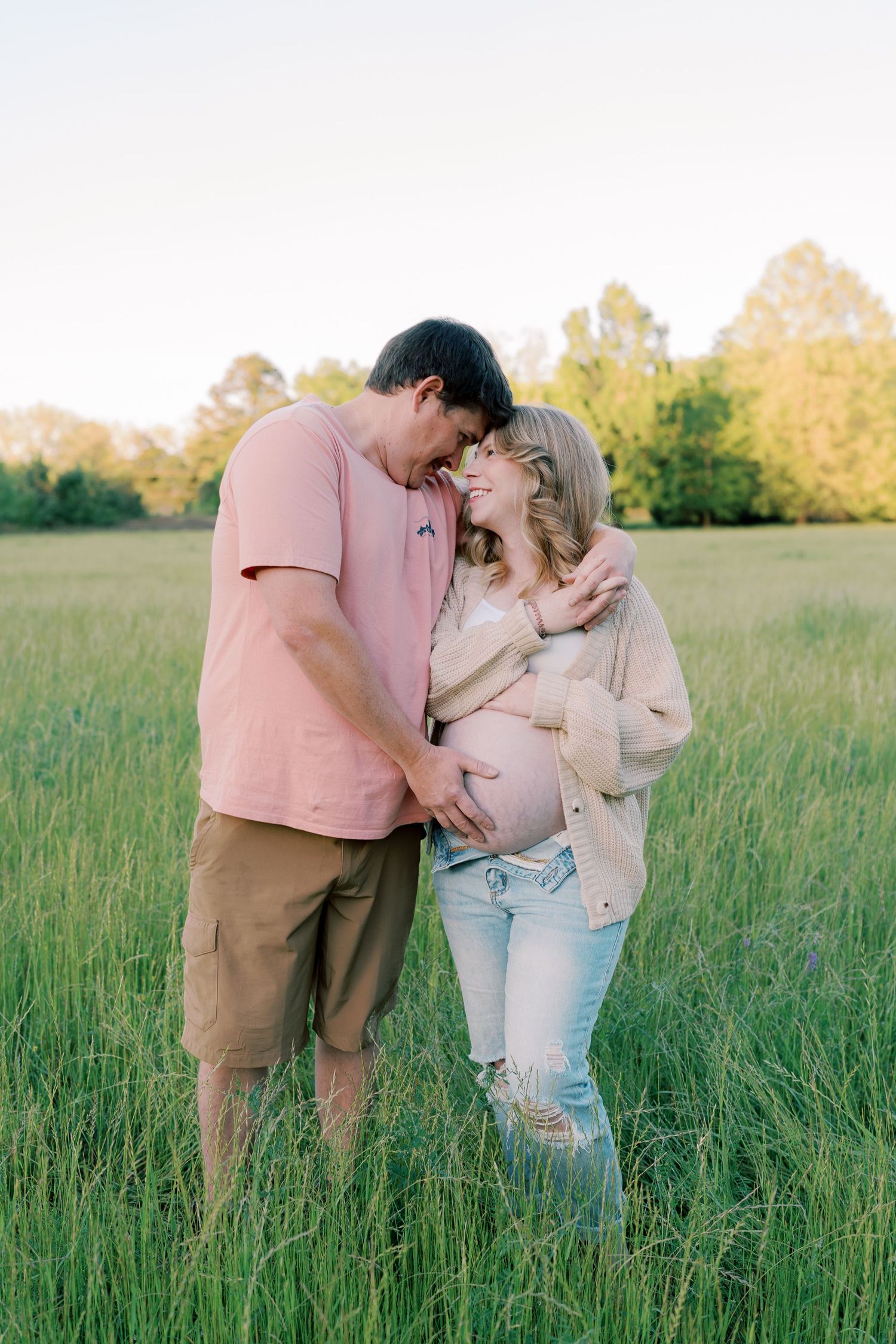 A romantic embrace captured in tall grass during sunset in an open field.