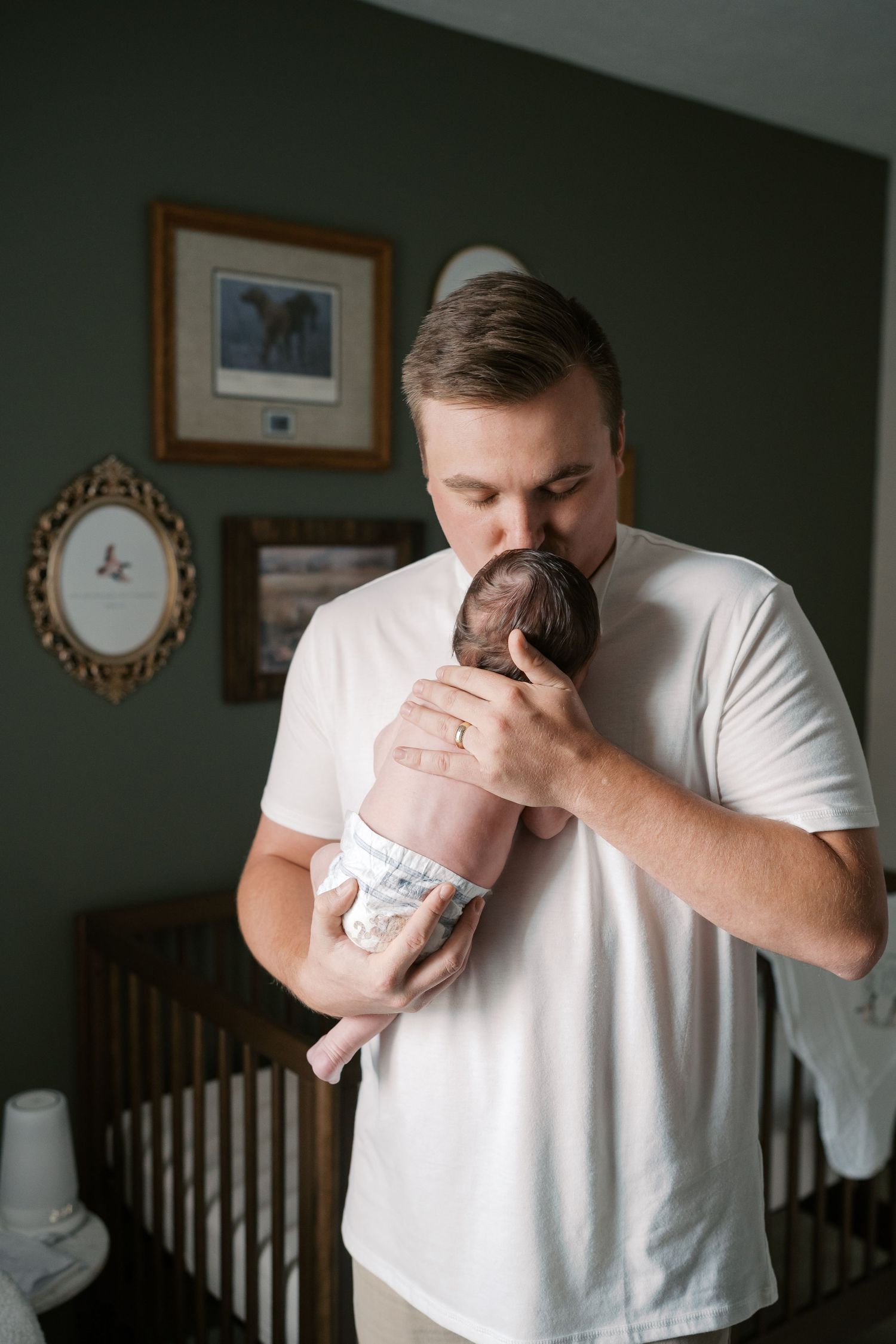 Emotional moment captured as a person in white shirt holds and kisses a newborn baby in a dimly lit room.