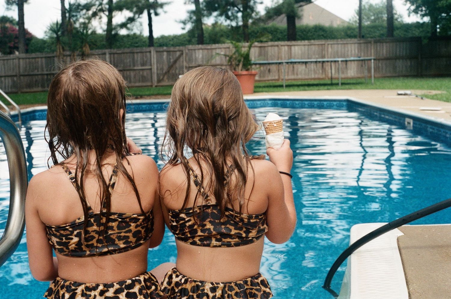 Two people in swimsuits lounging by a bright blue swimming pool on a sunny day.