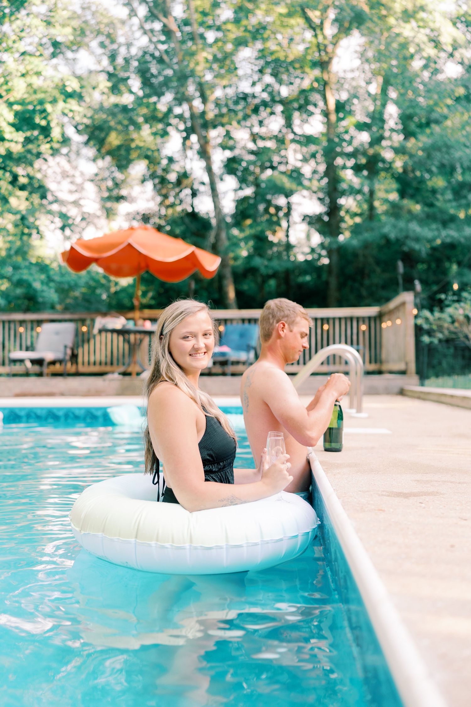Couple lounging on inflatable pool floats near a wooden deck.