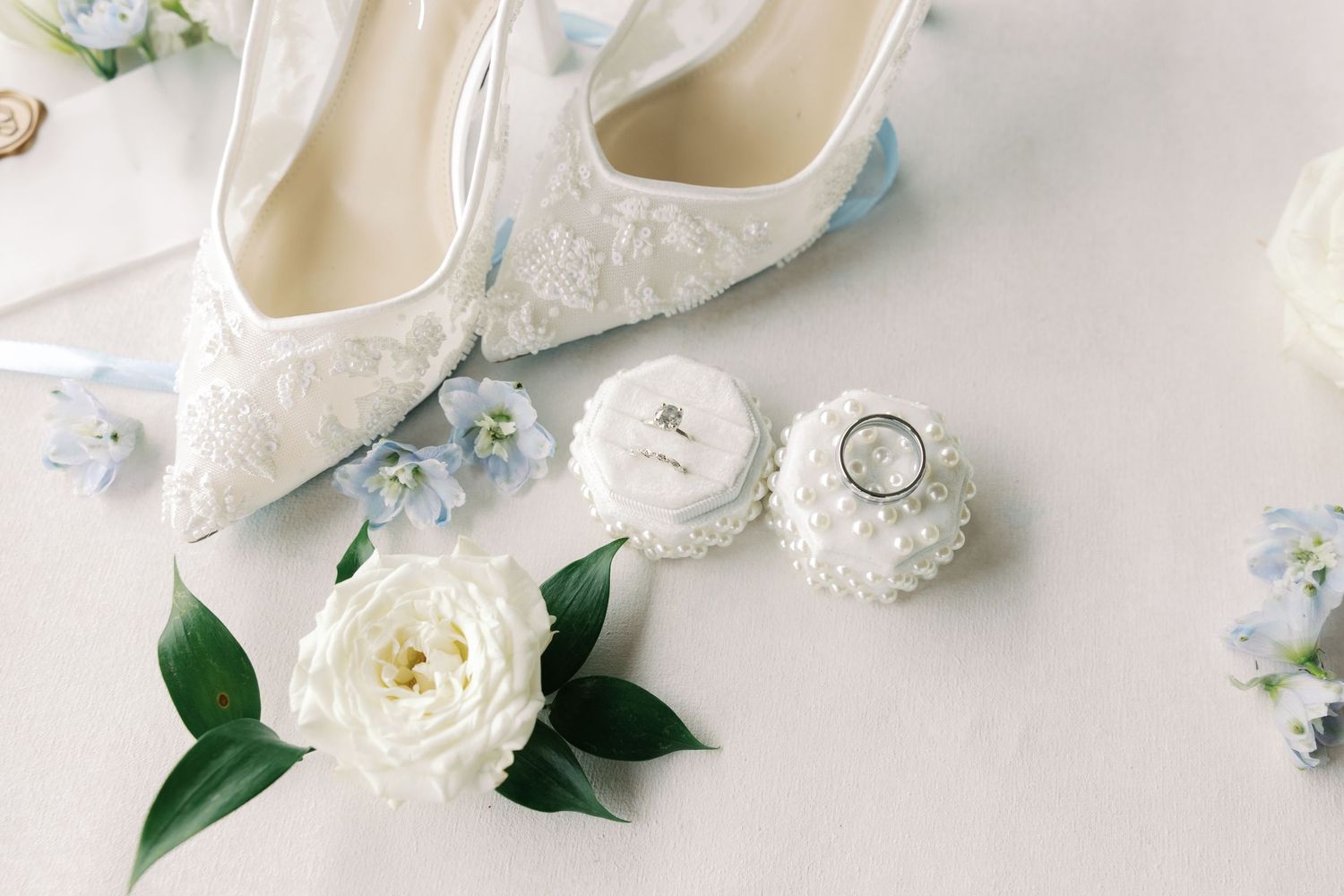 White wedding shoes with lace details surrounded by white ranunculus flowers and decorative elements.