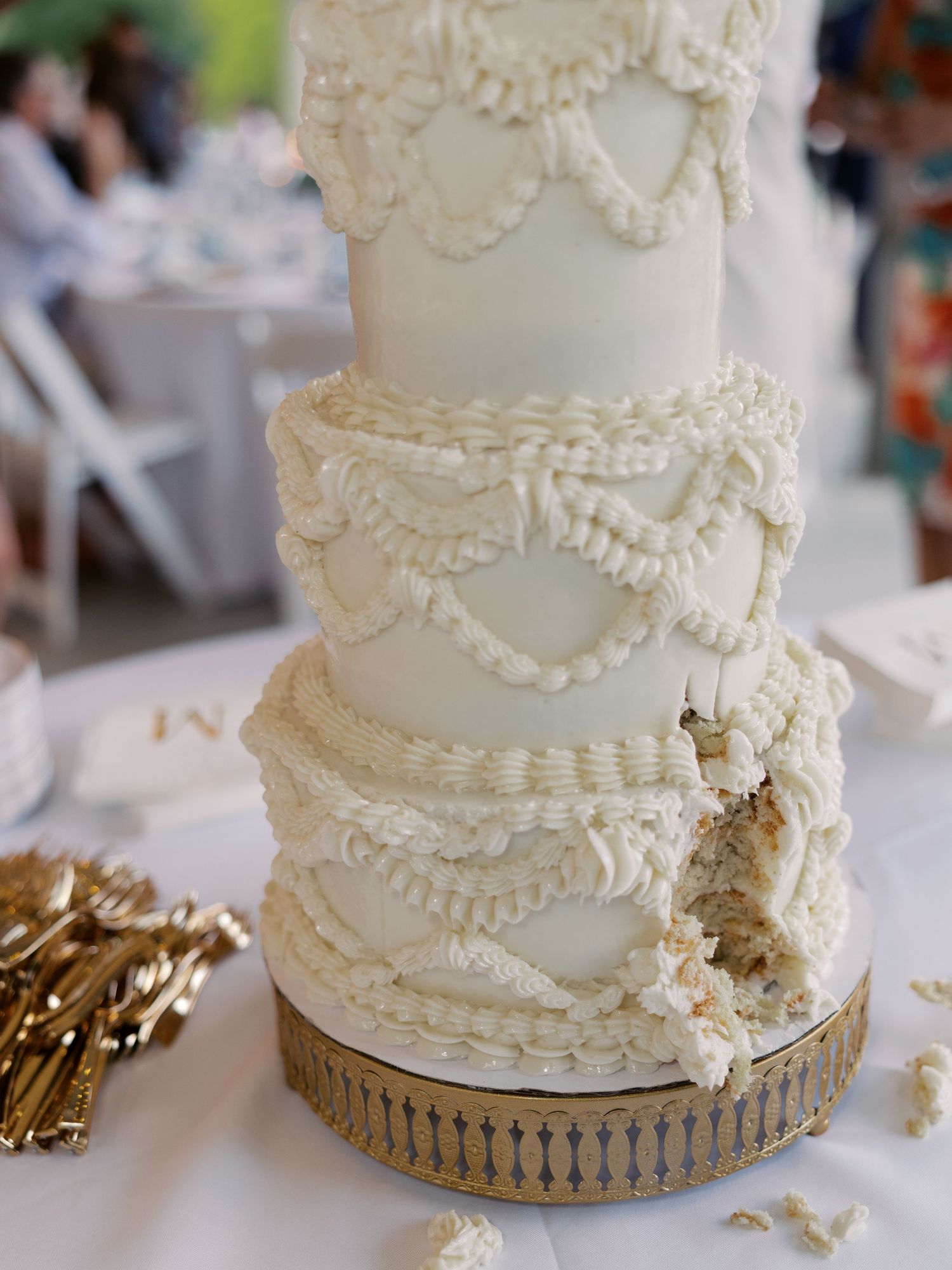 Close-up of white wedding cake with delicate piped details and gold accents.