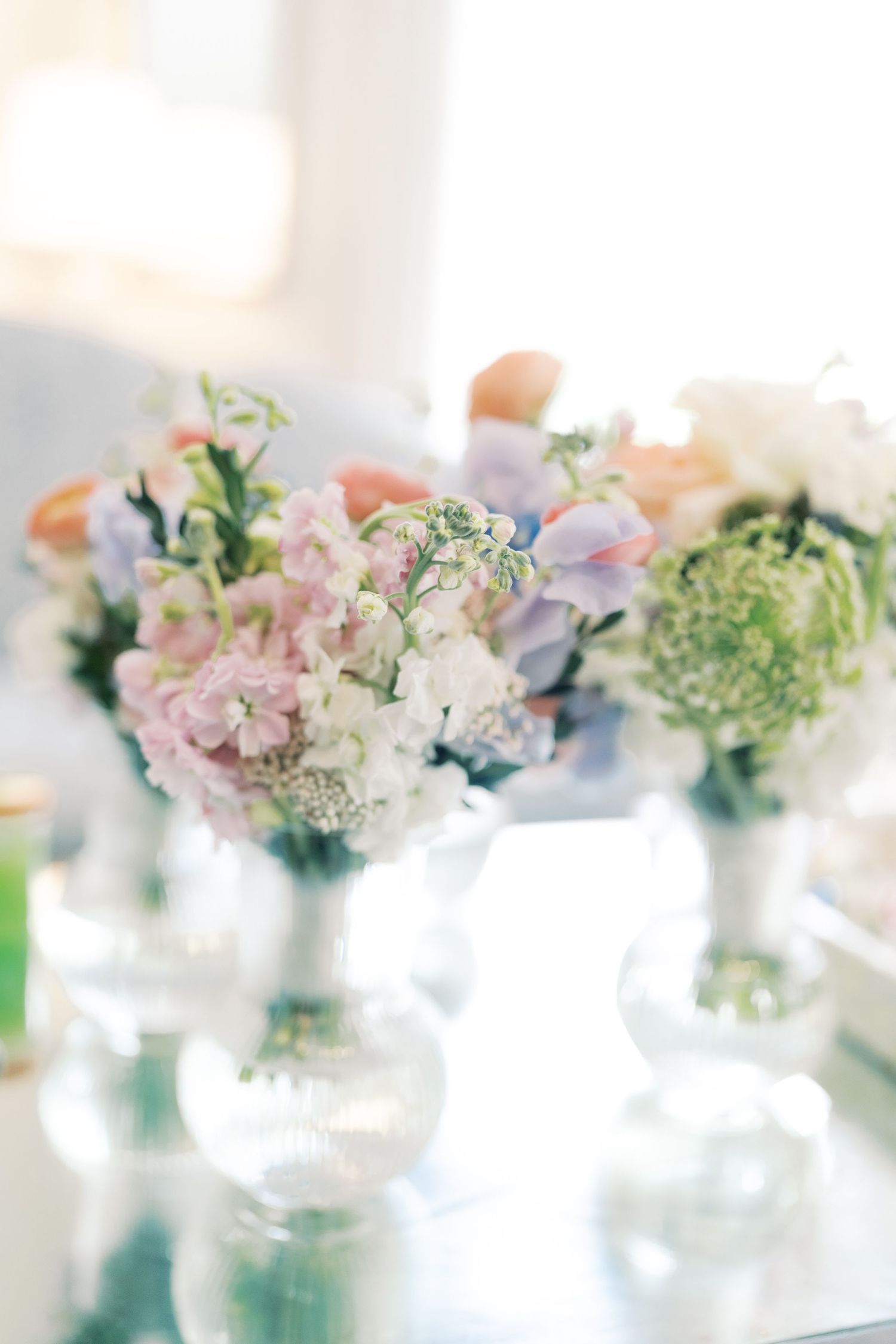 Delicate pastel floral arrangements in small glass vases create an elegant table setting.