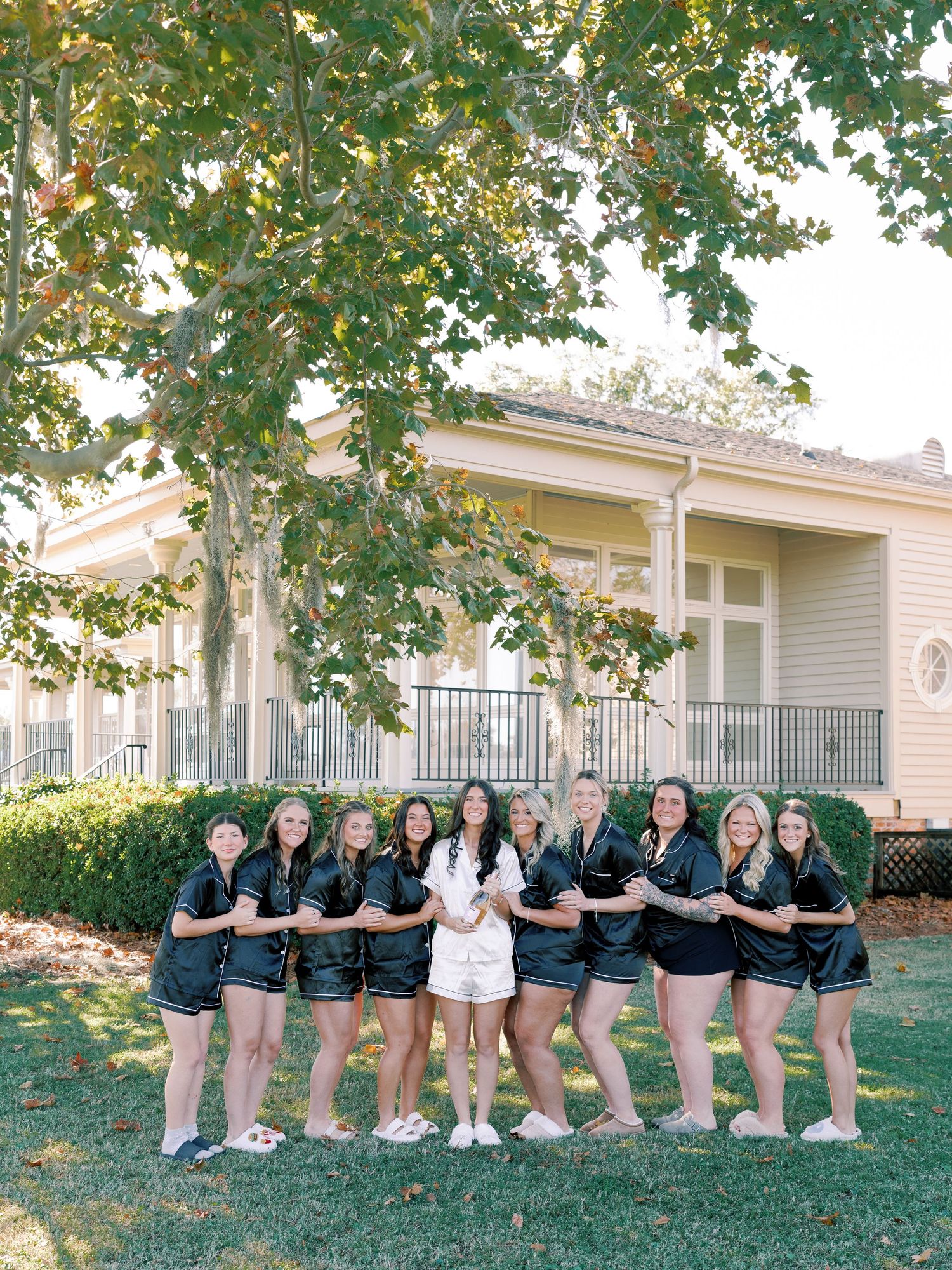 Wedding party lined up for photo outside elegant white house with wraparound porch.