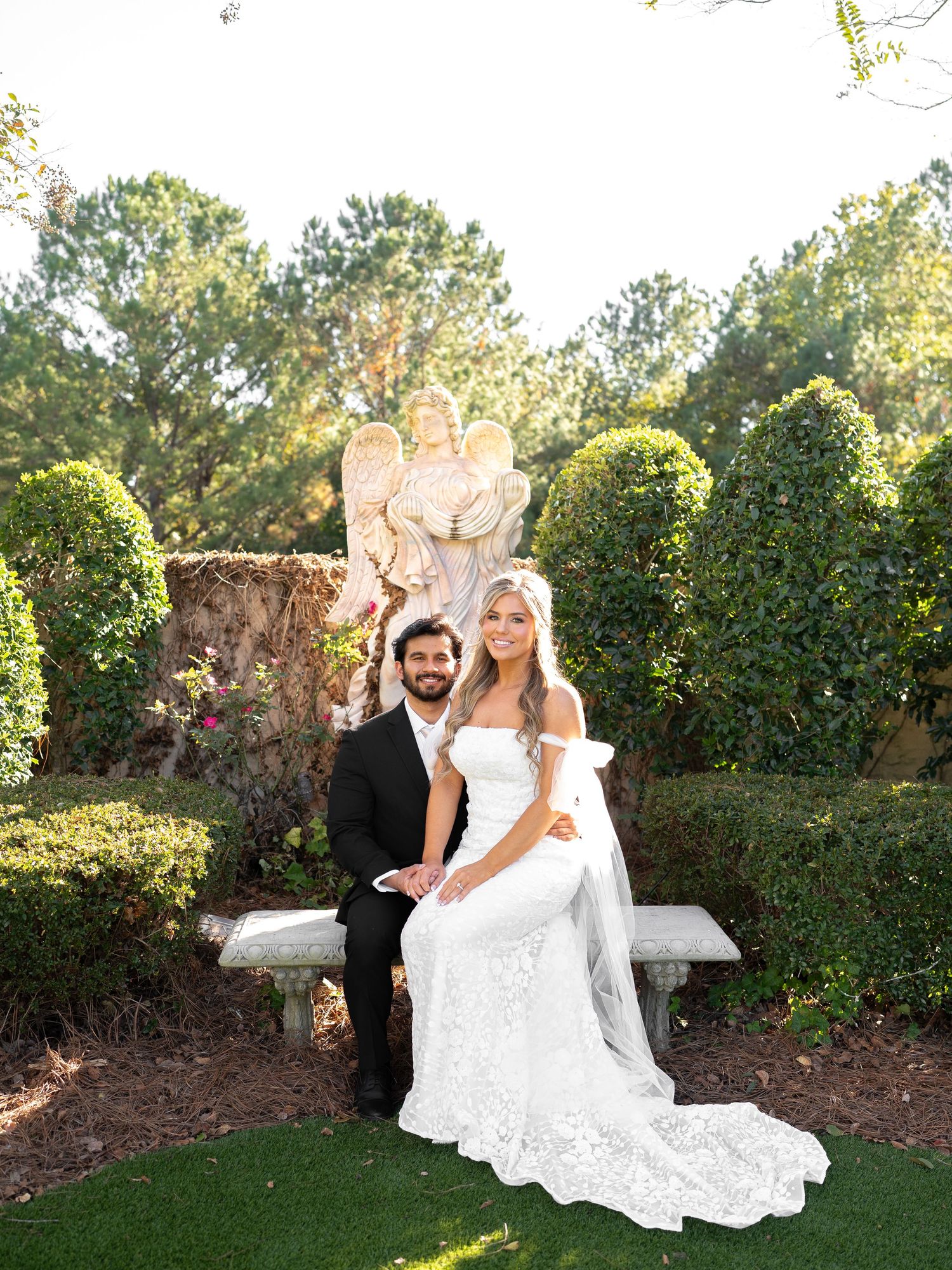 Wedding couple poses romantically on garden grounds with lush greenery backdrop.
