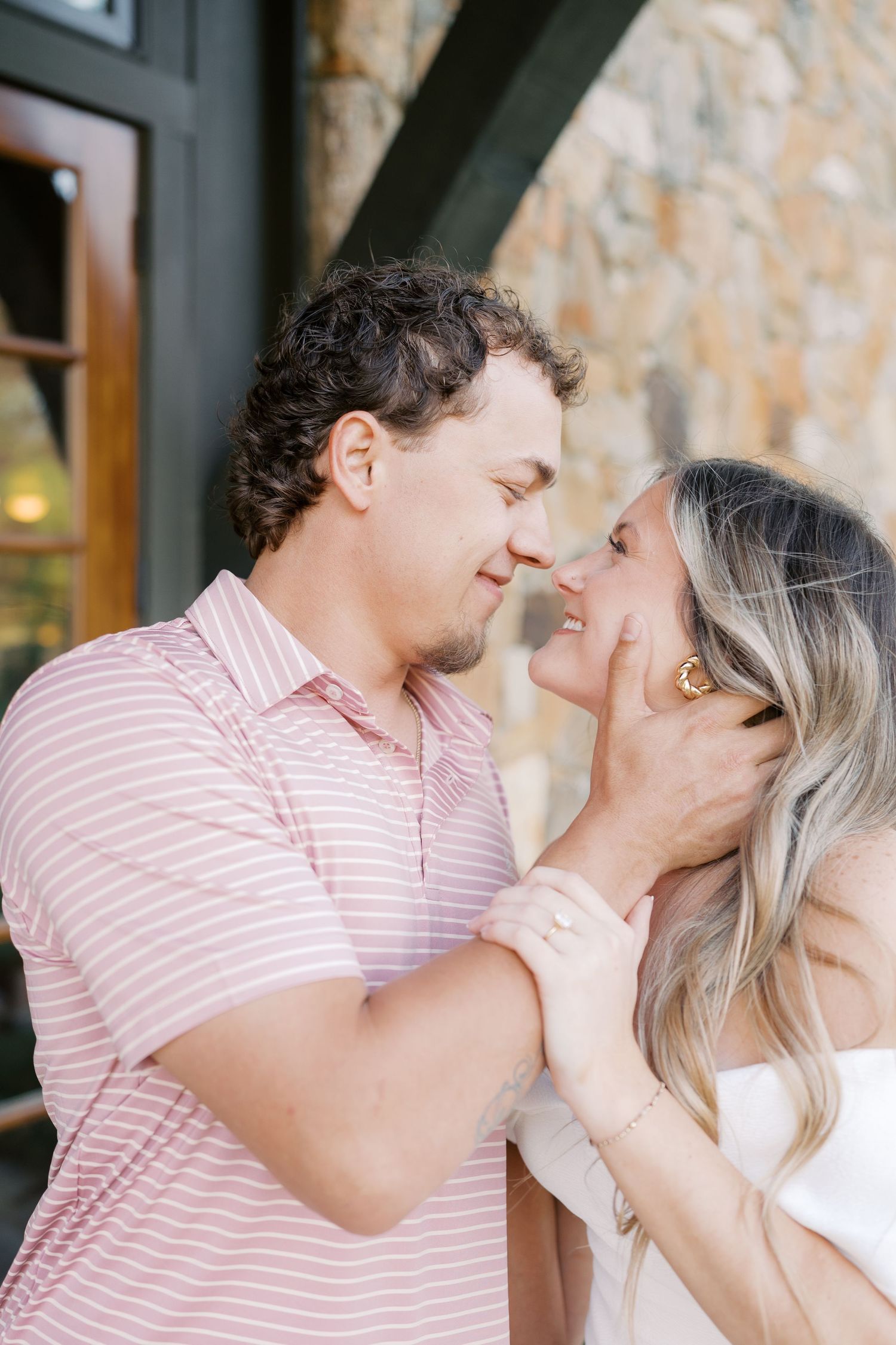Intimate moments captured between couple in pink and white against stone wall backdrop.