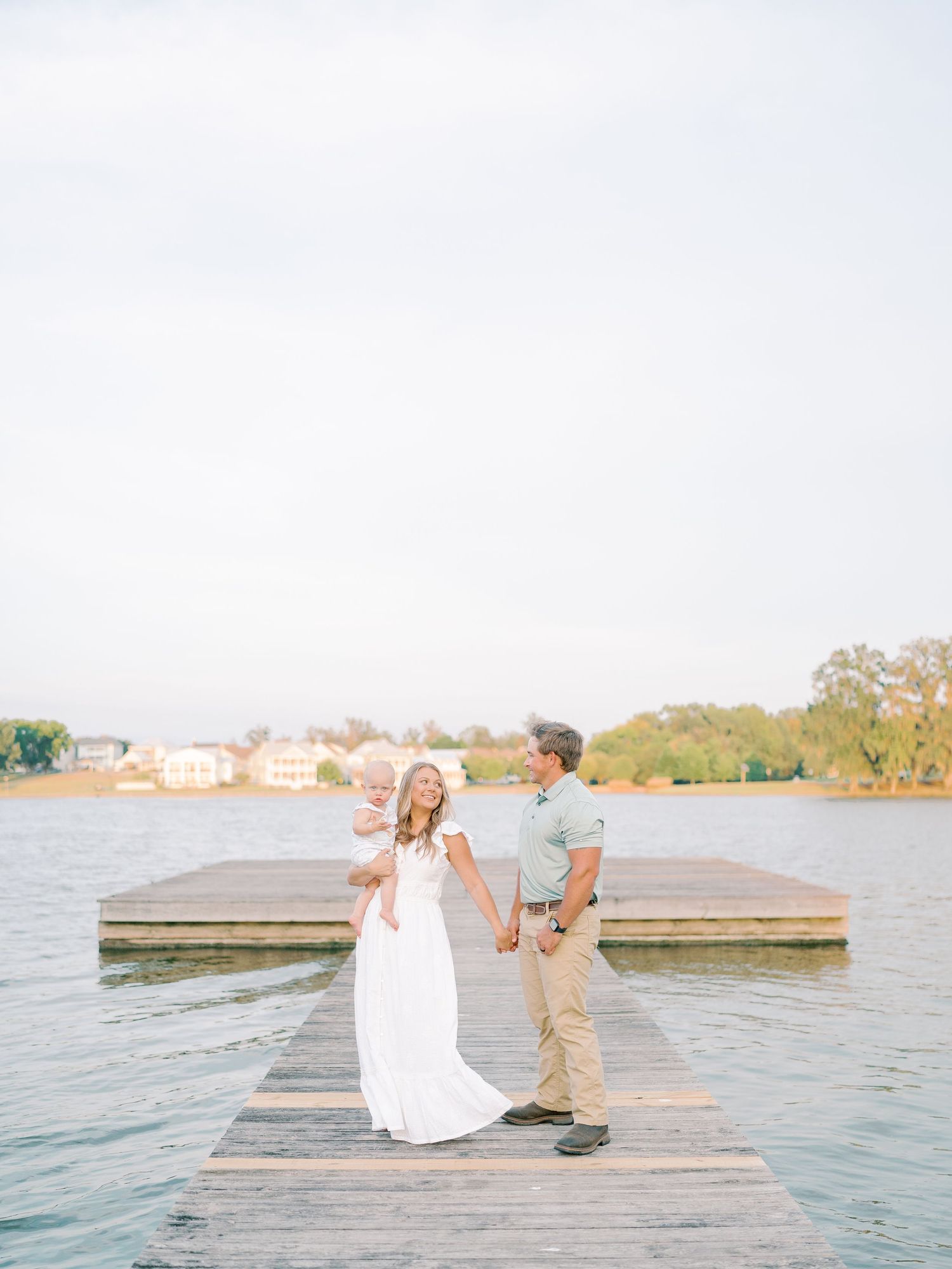 Family in white and tan outfits sharing joyful moments on a wooden dock by the water.